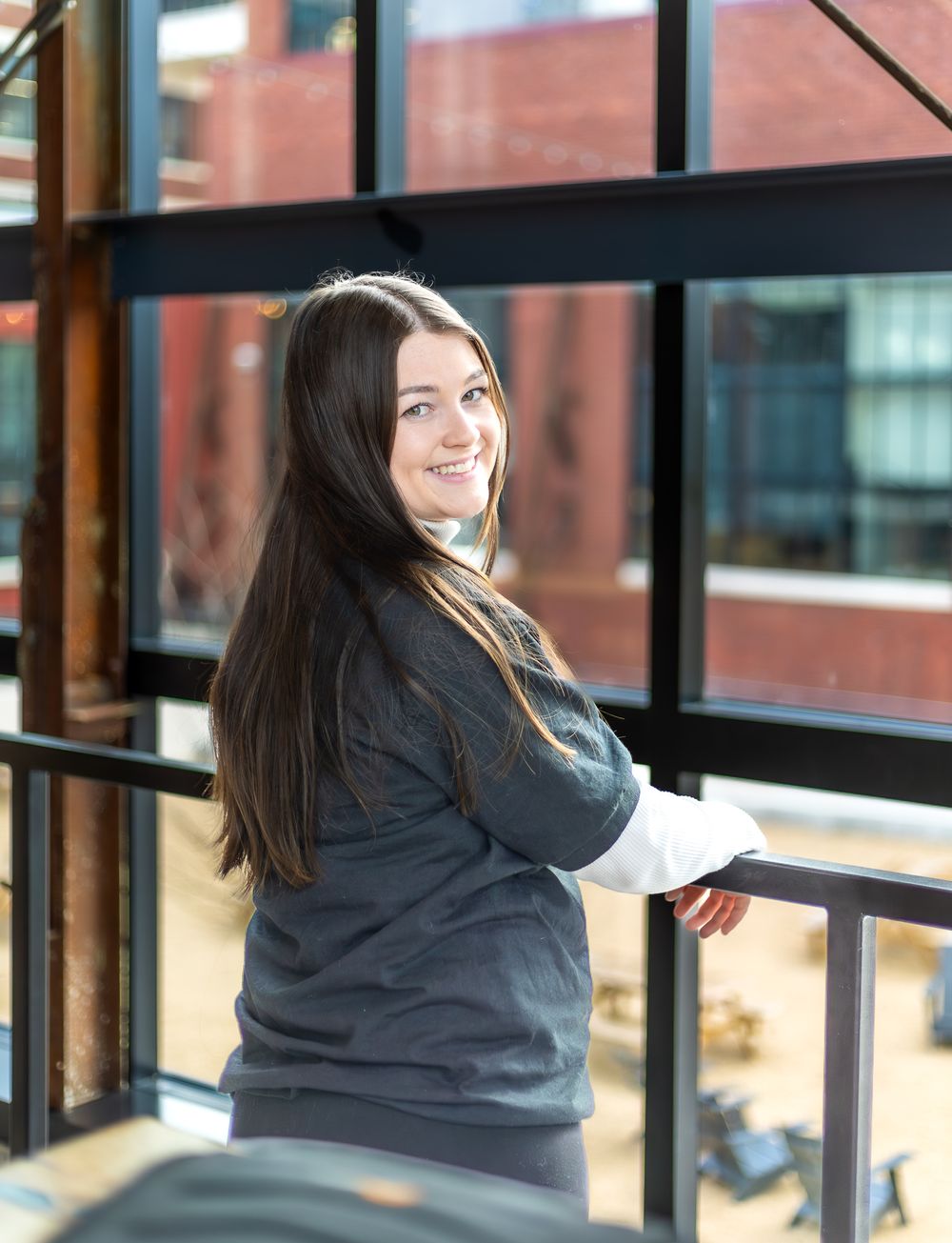 Employee in black uniform with white sleeves posing near windows in modern building interior.