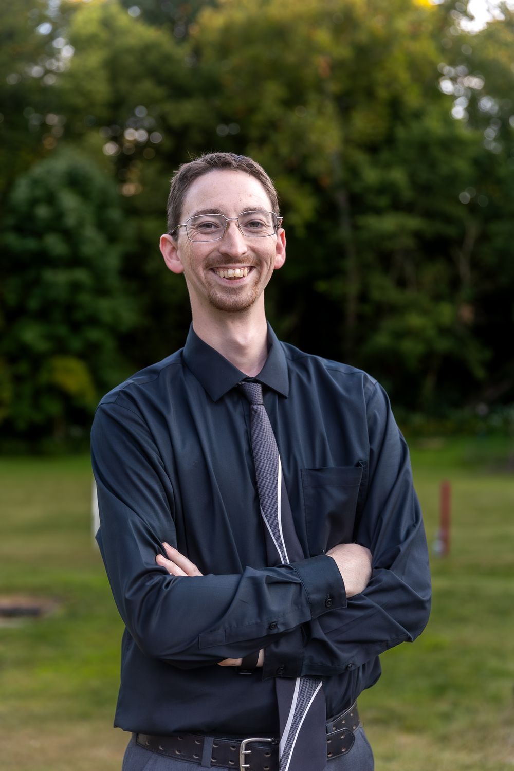 Professional portrait of someone in dark business attire standing outdoors.