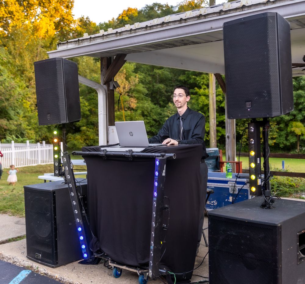 Professional DJ setup with speakers and lighting under a covered outdoor pavilion.
