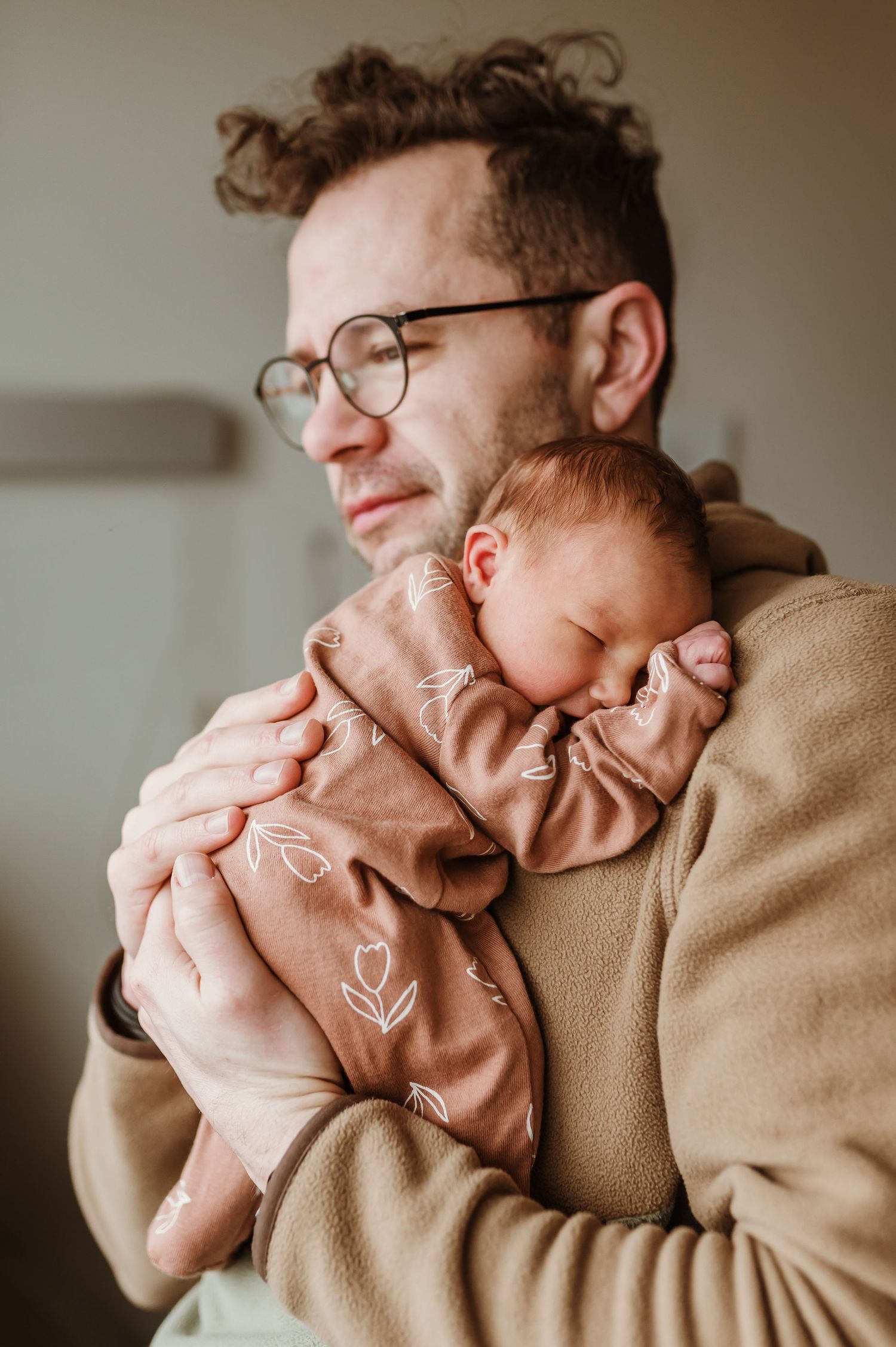 Baby in pink floral outfit sleeps peacefully against caregiver's shoulder.