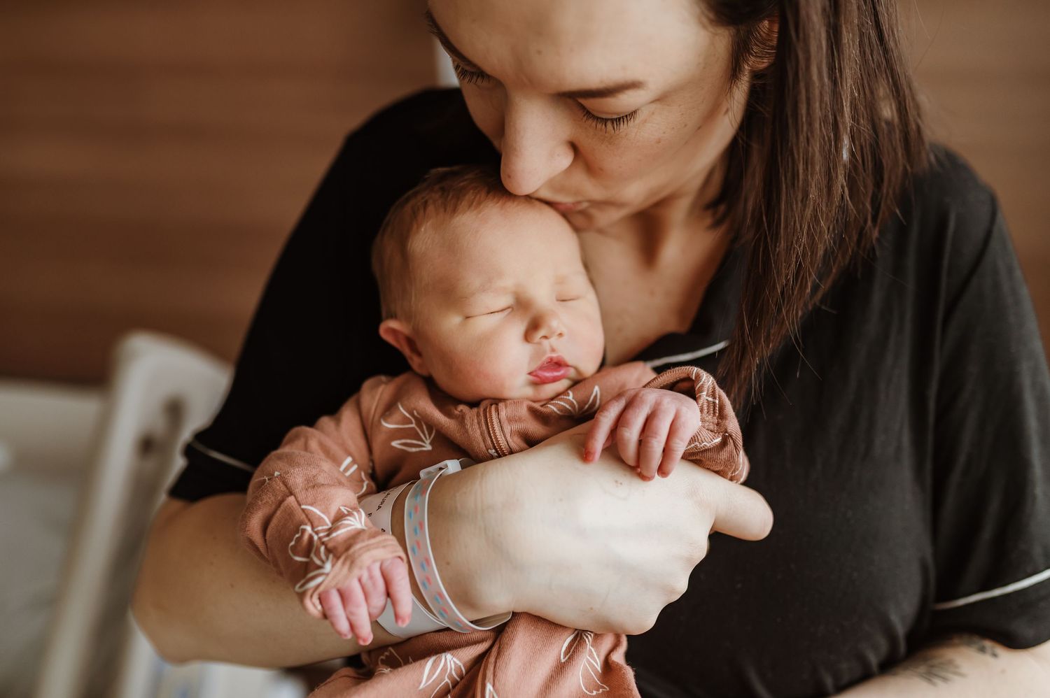 Newborn in pink outfit rests peacefully during intimate bonding moment.