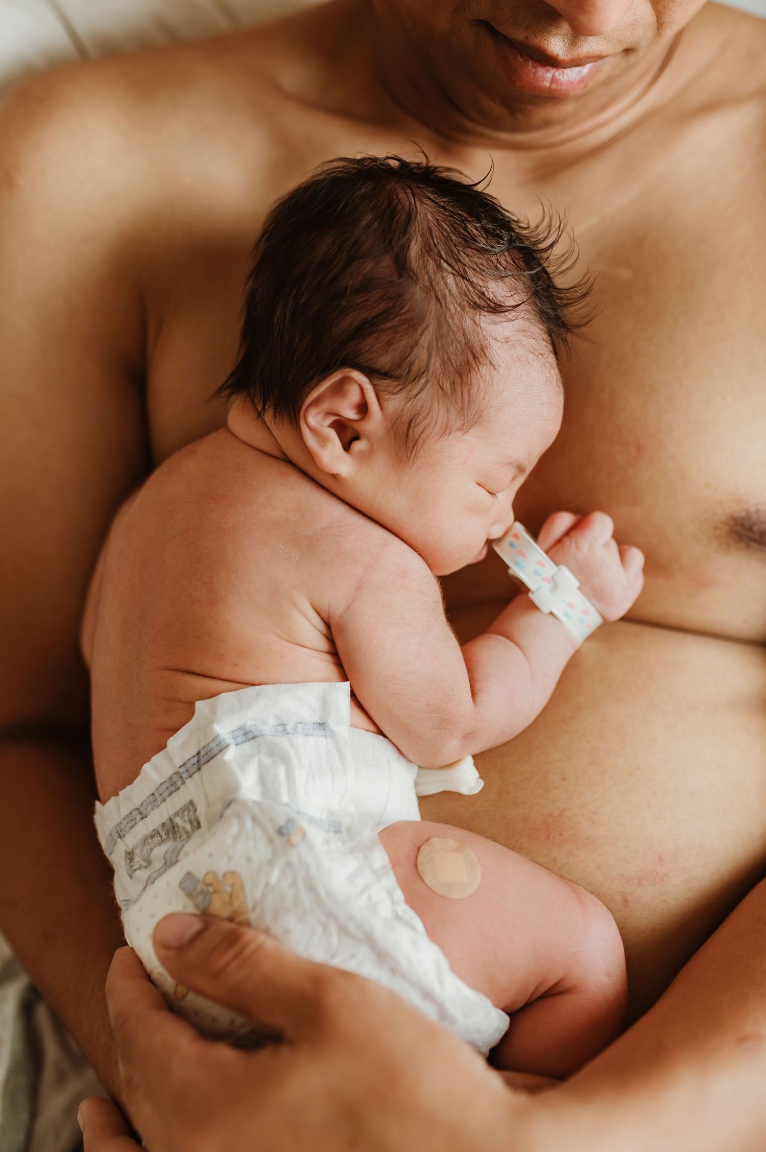Newborn baby rests peacefully while being held against bare skin in intimate bonding moment.
