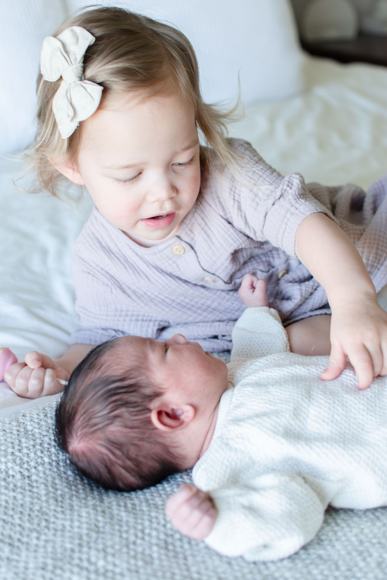Big sister tickles her younger sister's belly as they lay on the bed.