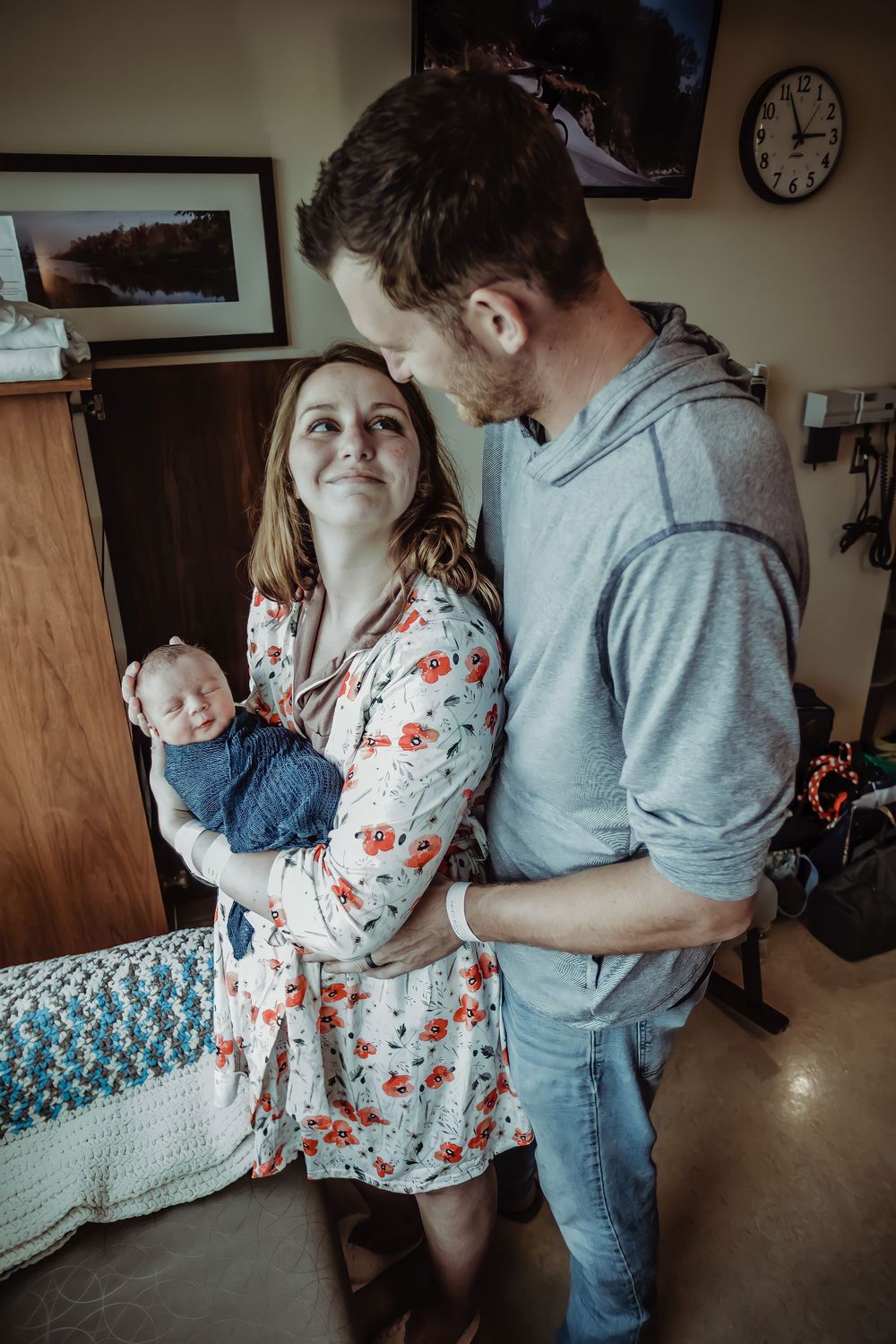 Parents sharing an intimate moment while holding their newborn baby in a hospital room.