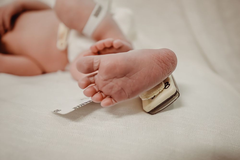 Close-up shot of tiny newborn baby feet against white hospital bedding.
