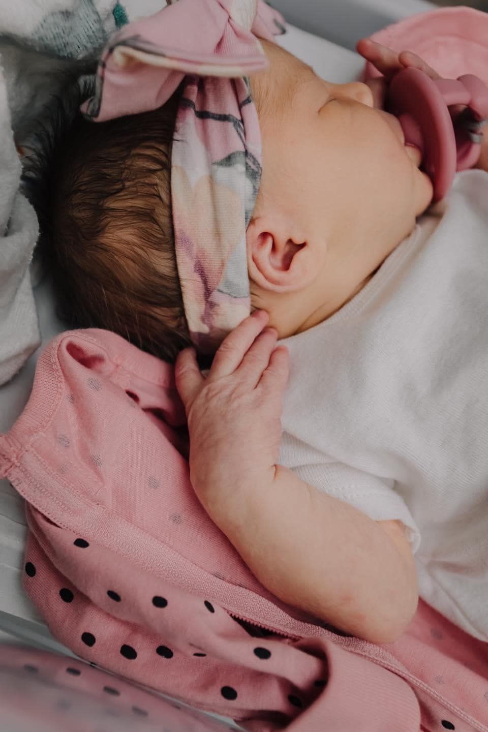 Sleeping newborn baby wearing pink polka dot clothing.
