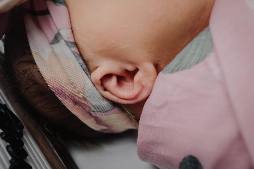 Close-up view of a tiny baby's ear against pink floral fabric.