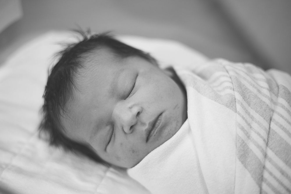 Black and white portrait of peaceful sleeping newborn wrapped in white blanket.