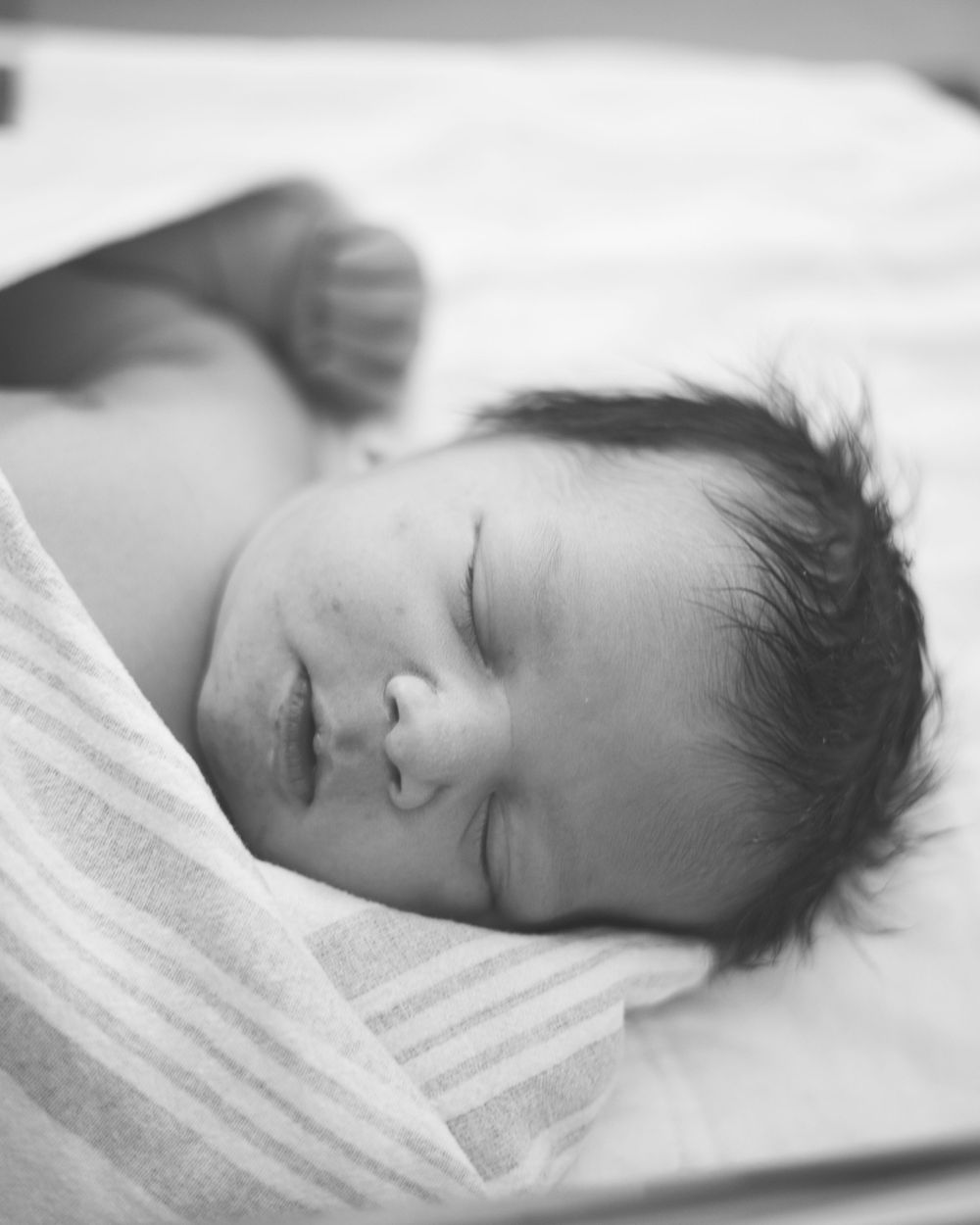 Black and white close-up of sleeping newborn wrapped in soft textured blanket.