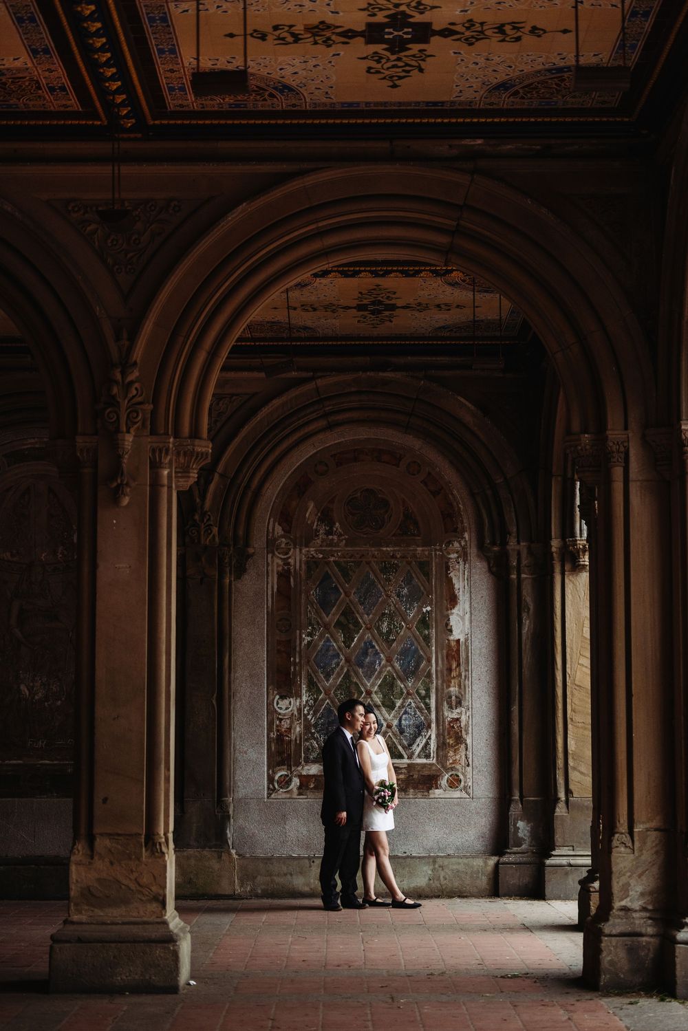 An elegant wedding portrait in a historic hallway with ornate architecture and stained glass windows.