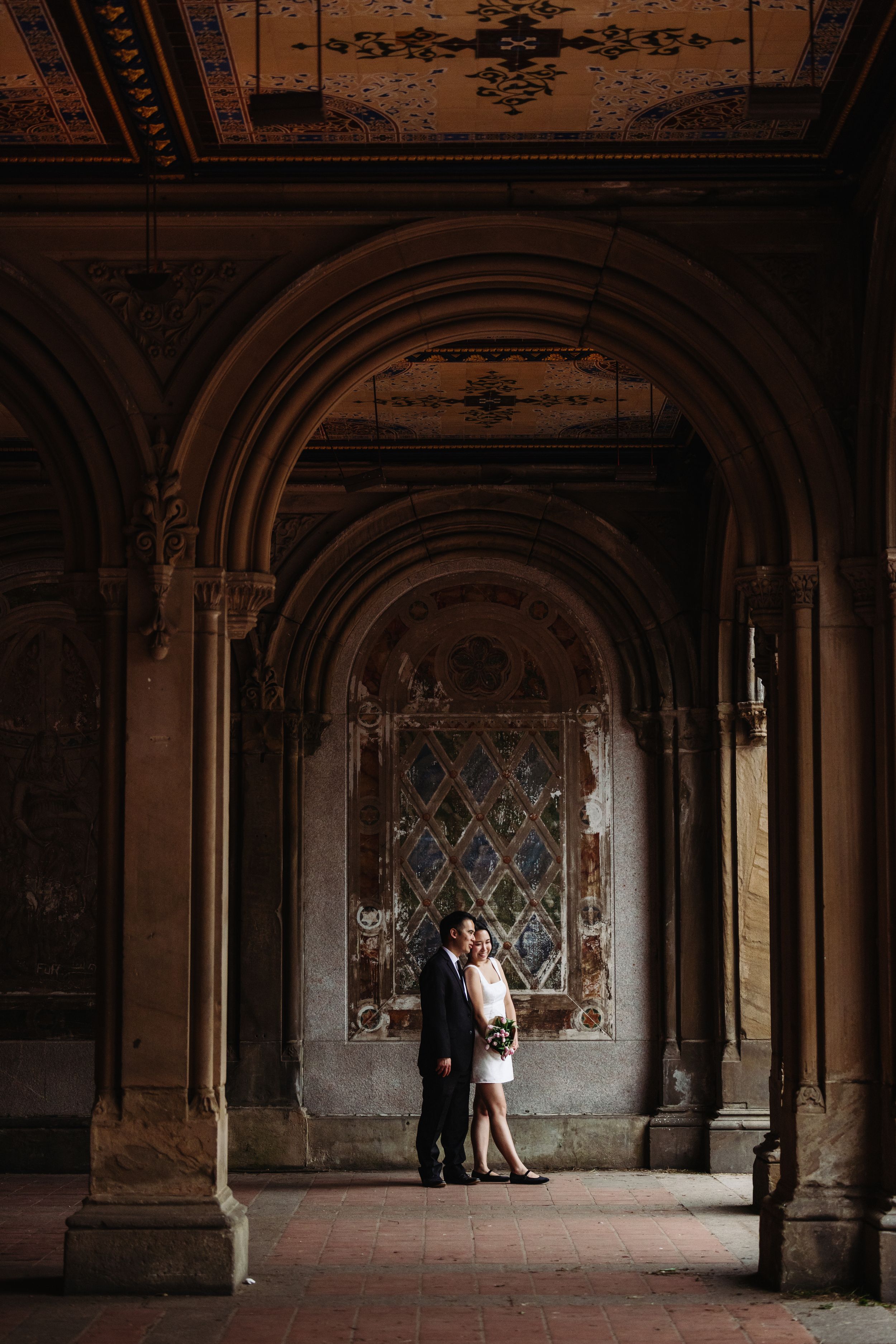 An elegant wedding portrait in a historic hallway with ornate architecture and stained glass windows.