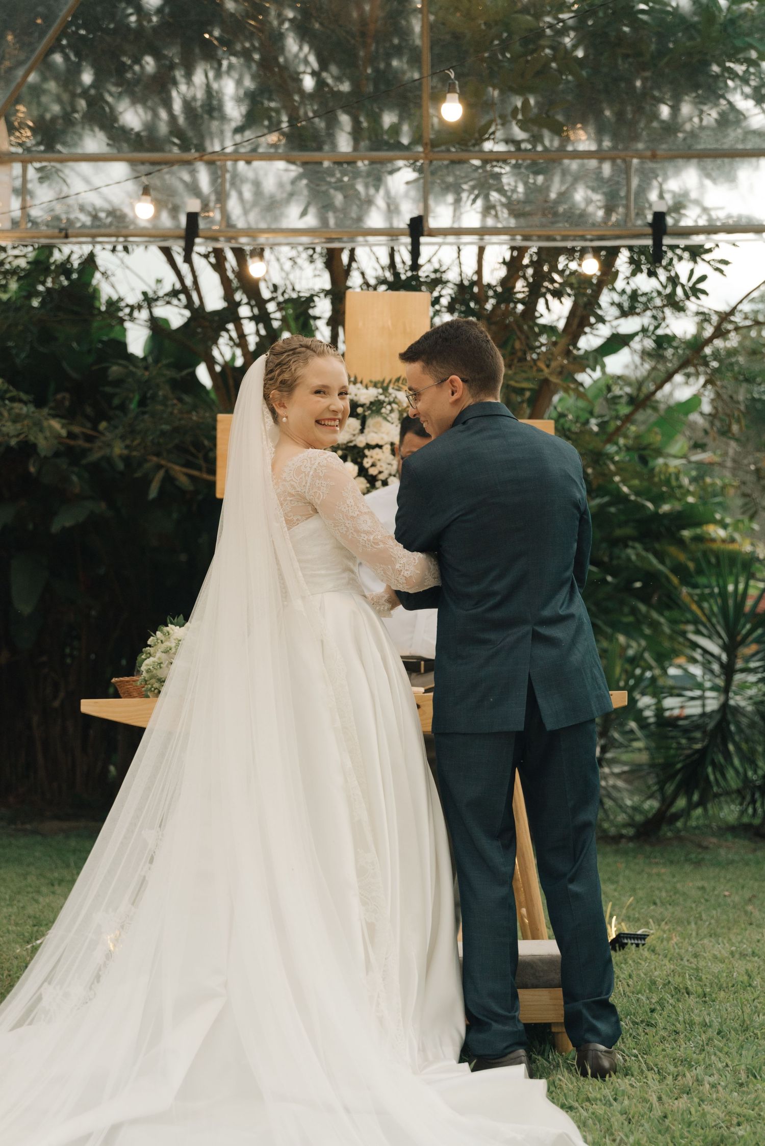 A romantic outdoor wedding ceremony captured as the couple shares their first kiss under string lights and greenery.