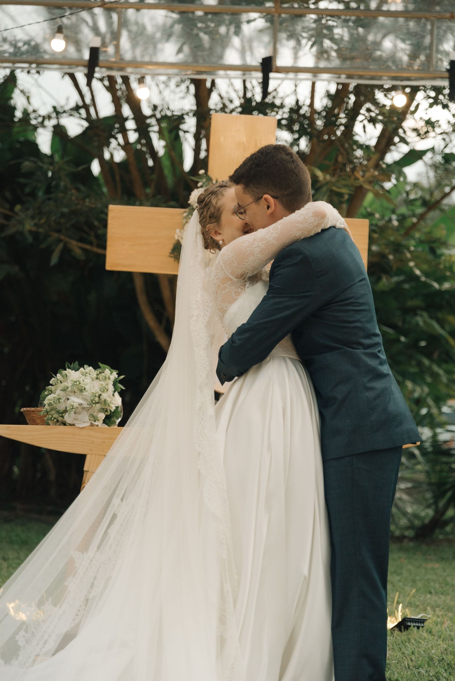 Bride in a flowing white gown embraces groom during intimate outdoor garden wedding ceremony.