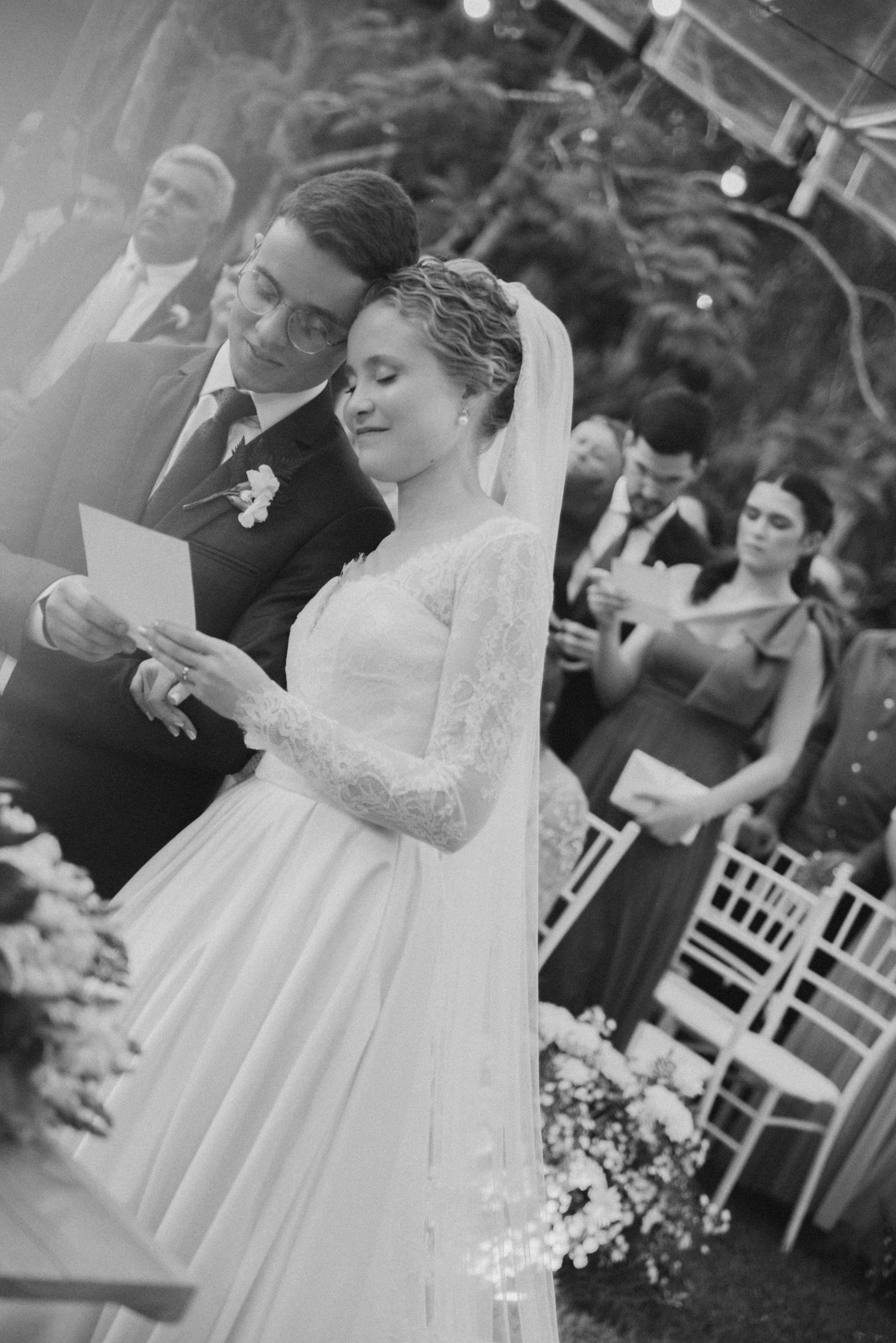 Black and white photo of wedding ceremony with guests seated in garden setting.
