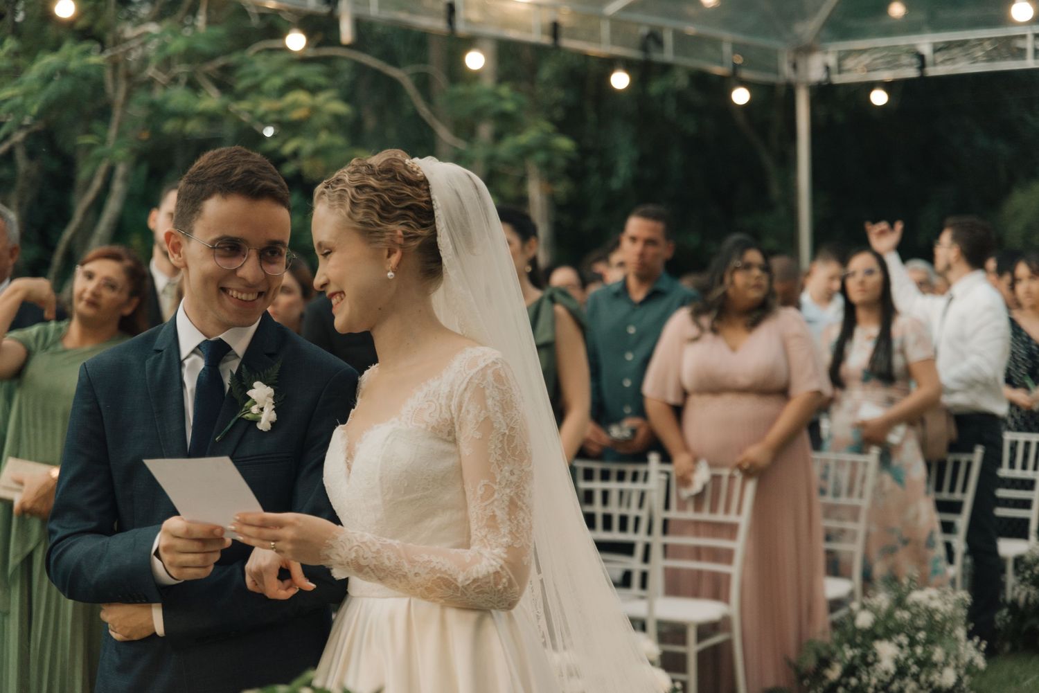 Wedding ceremony in lush garden setting with string lights and guests in attendance.