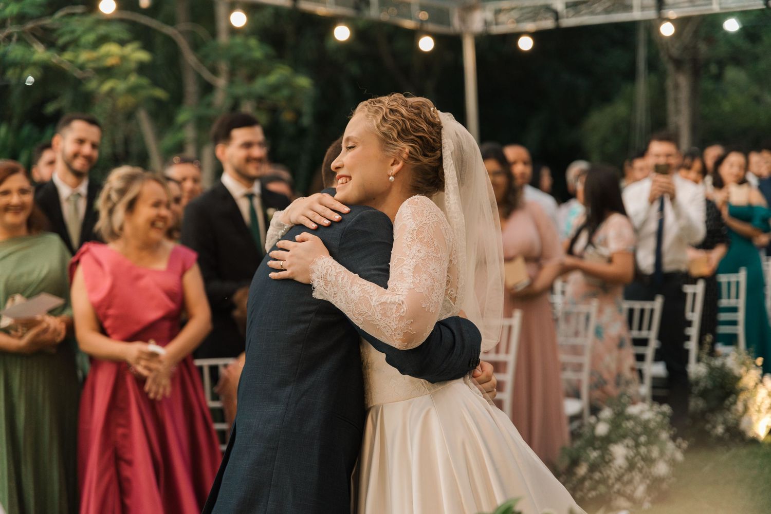 Emotional embrace during garden wedding ceremony while guests look on with joy.