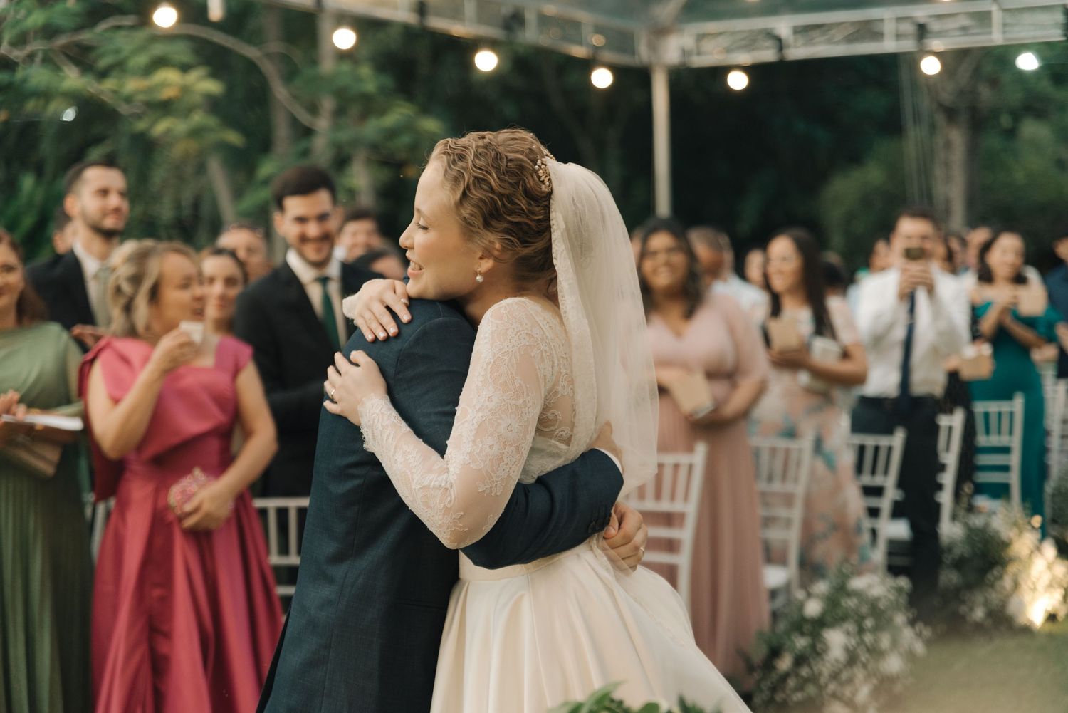 Wedding celebration in outdoor garden venue with guests watching emotional moment.