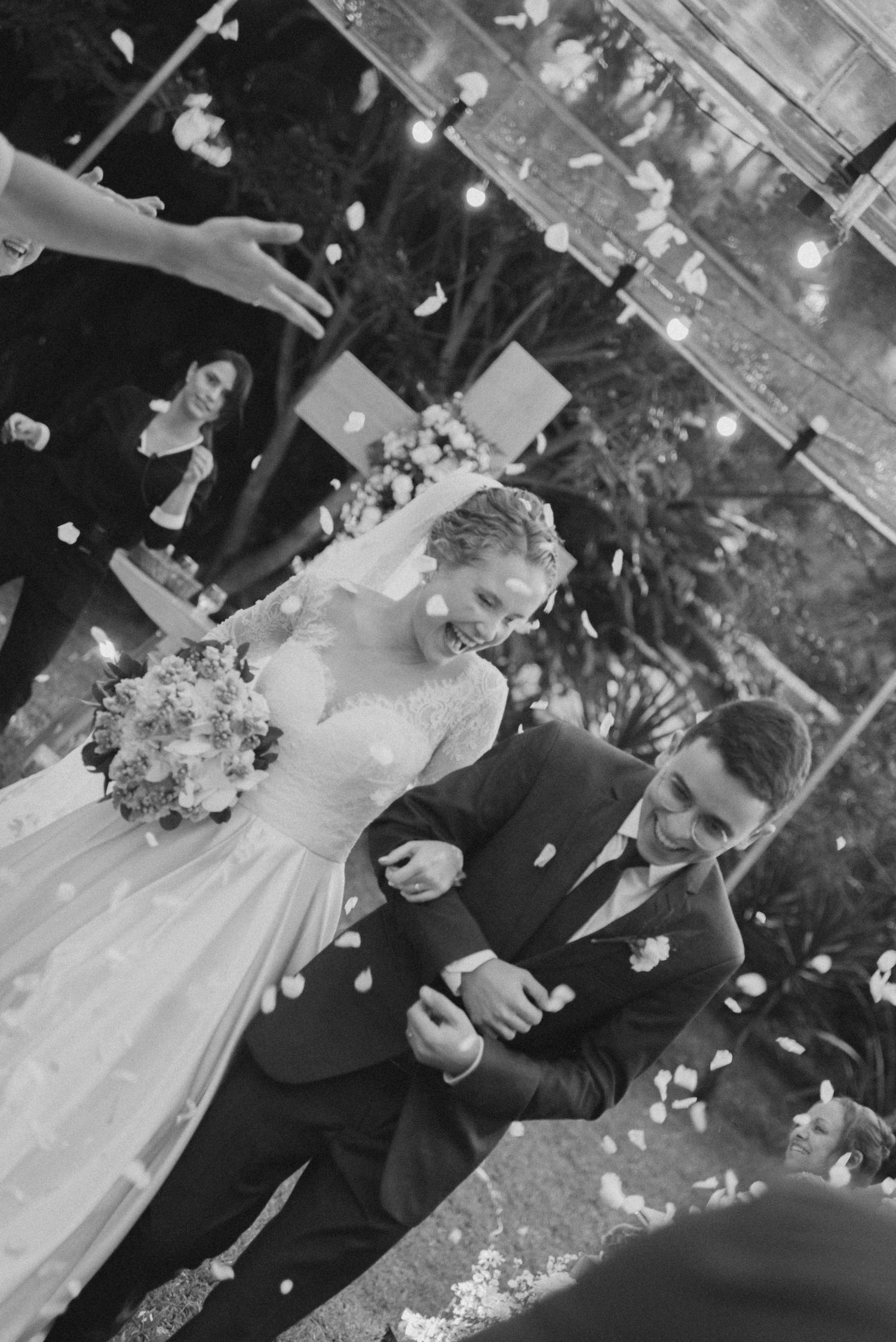 A couple walks down the aisle while guests shower them with petals during their wedding celebration.