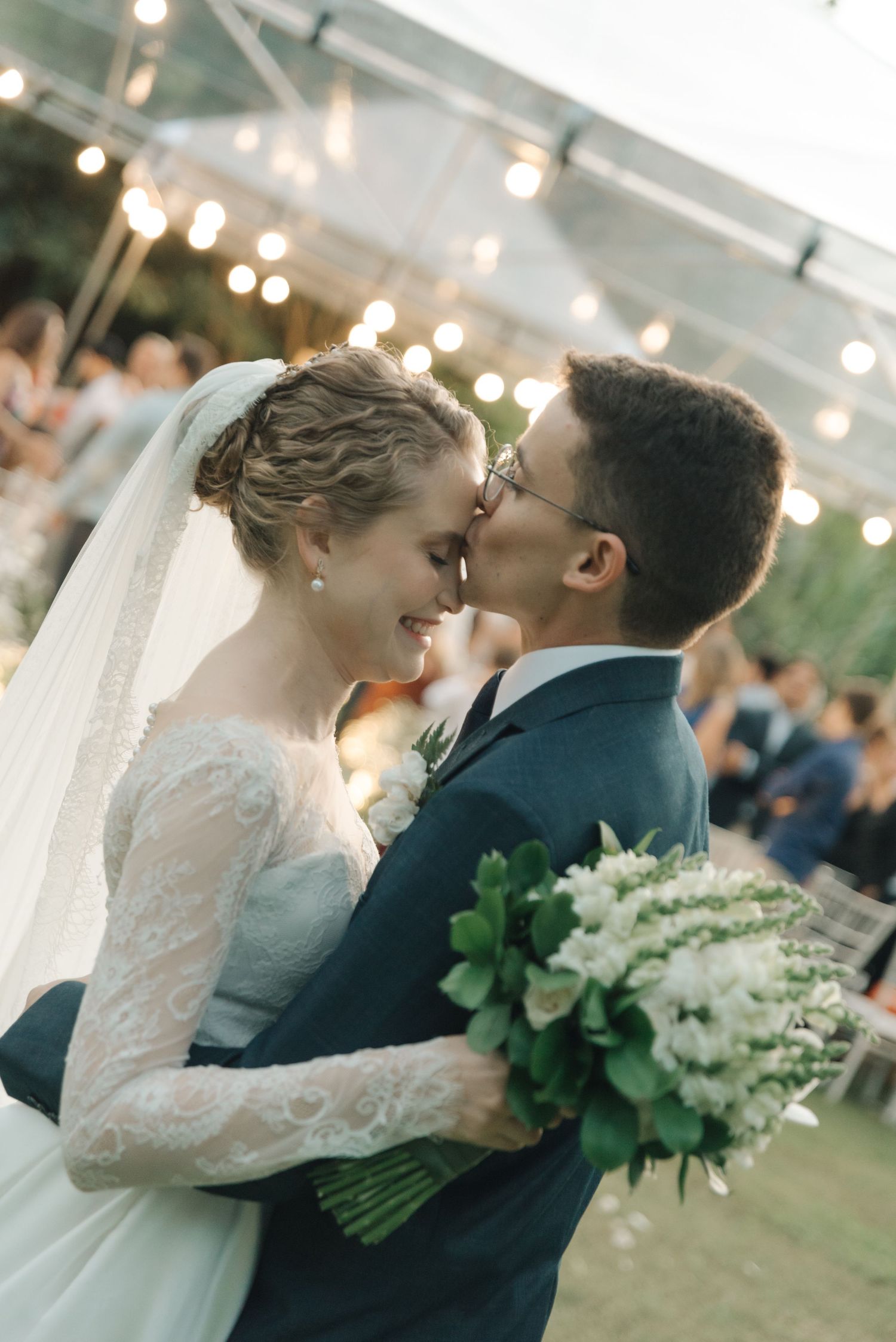 Romantic moment between newlyweds under glowing tent lights at sunset wedding reception.