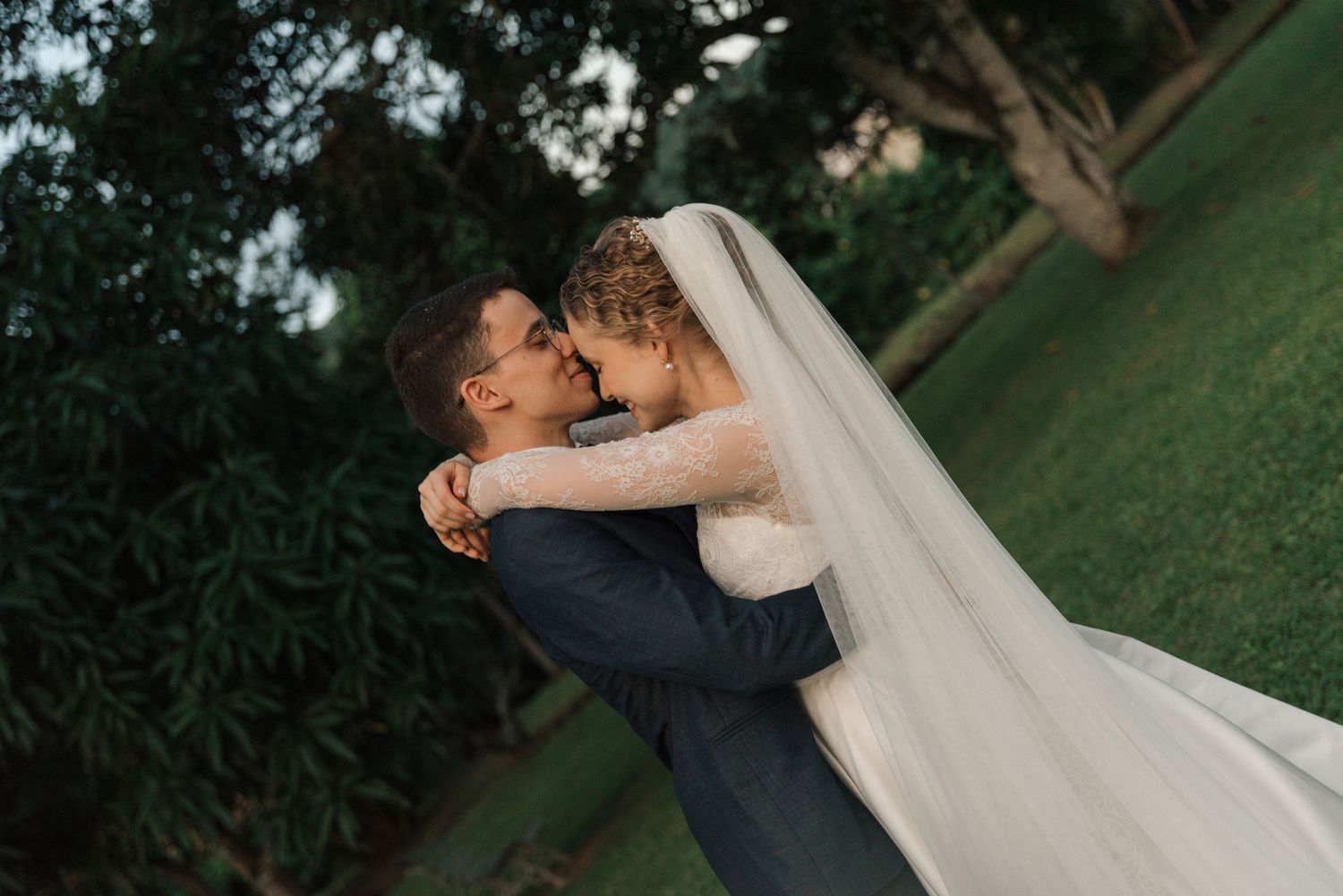 Newlyweds share an intimate embrace on a grassy lawn during their wedding photoshoot.
