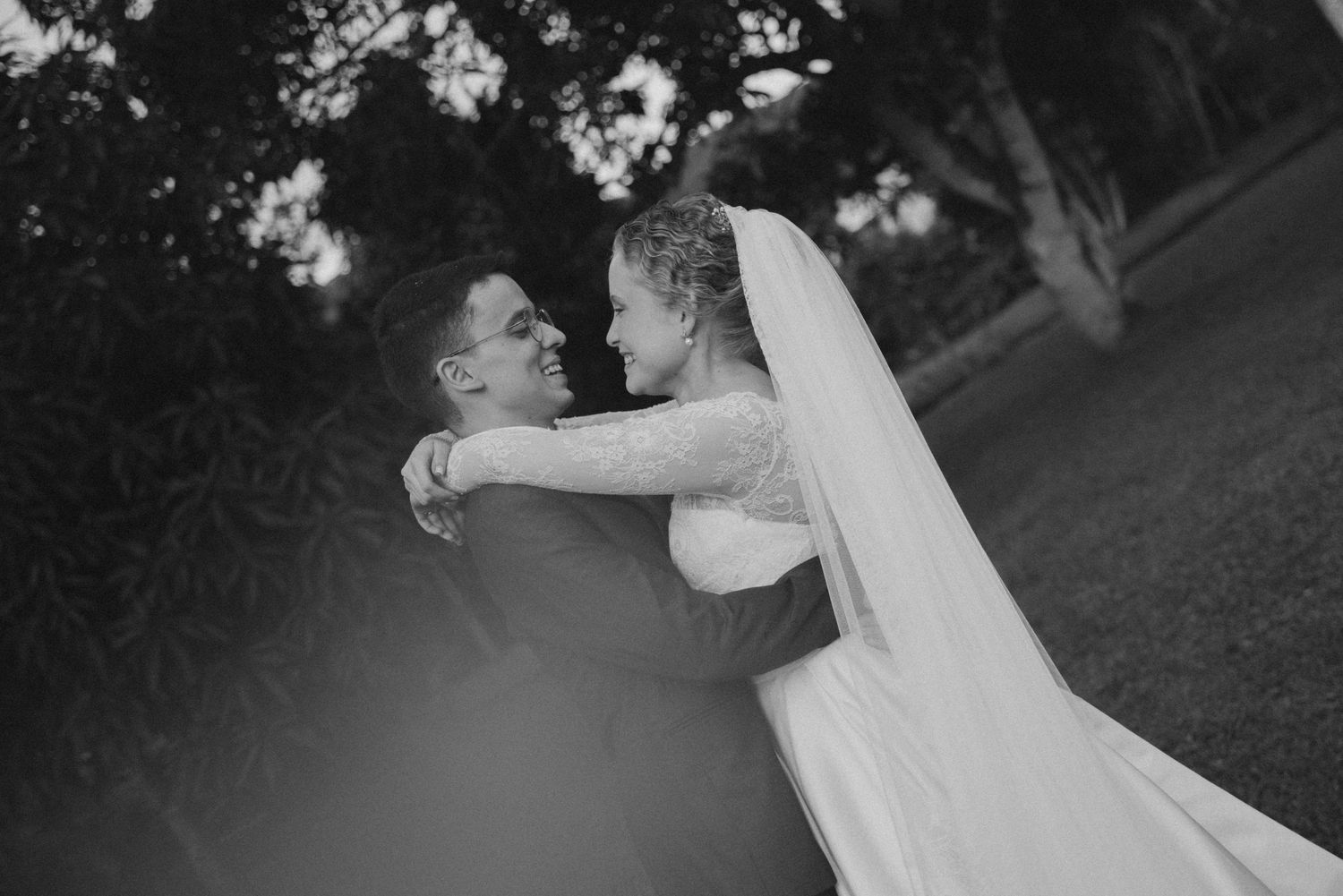 Black and white portrait of newlyweds sharing intimate embrace during outdoor wedding celebration.