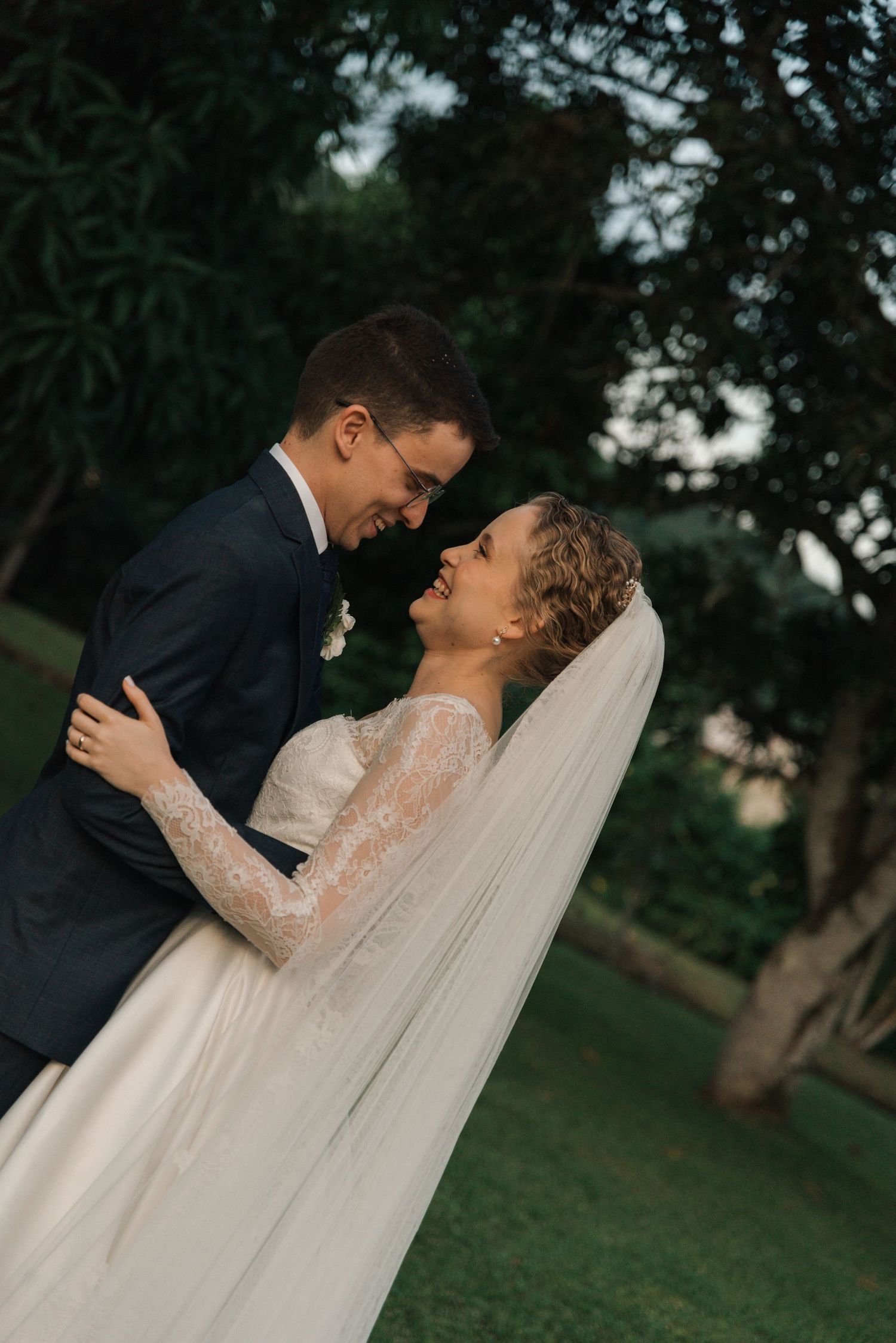 Joyful wedding couple sharing a romantic moment outdoors with flowing veil.
