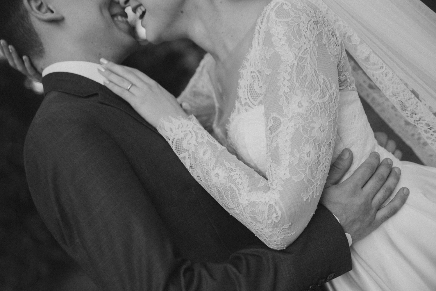 Black and white close-up of bride in lace sleeves embracing groom.