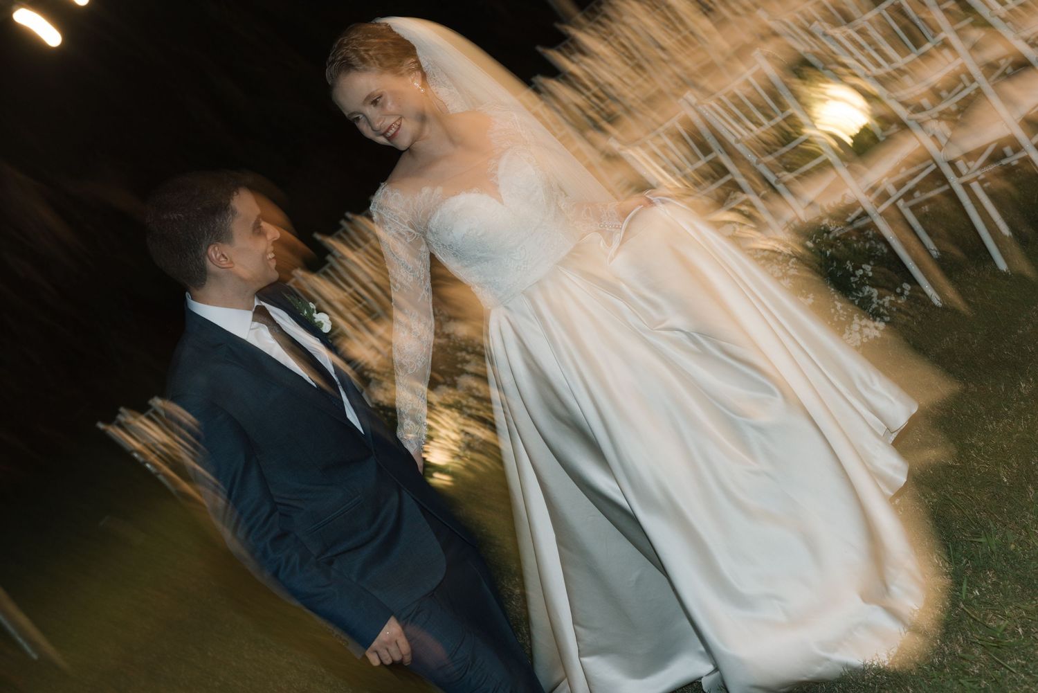 Motion-blur wedding photo of couple dancing under outdoor lighting.