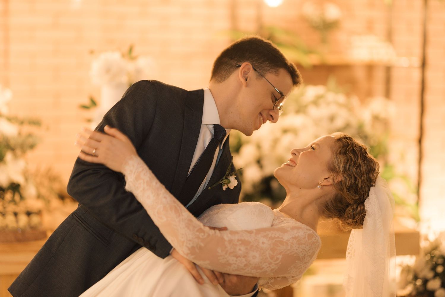 A romantic slow dance at a wedding reception with soft amber lighting and flowing white dress.