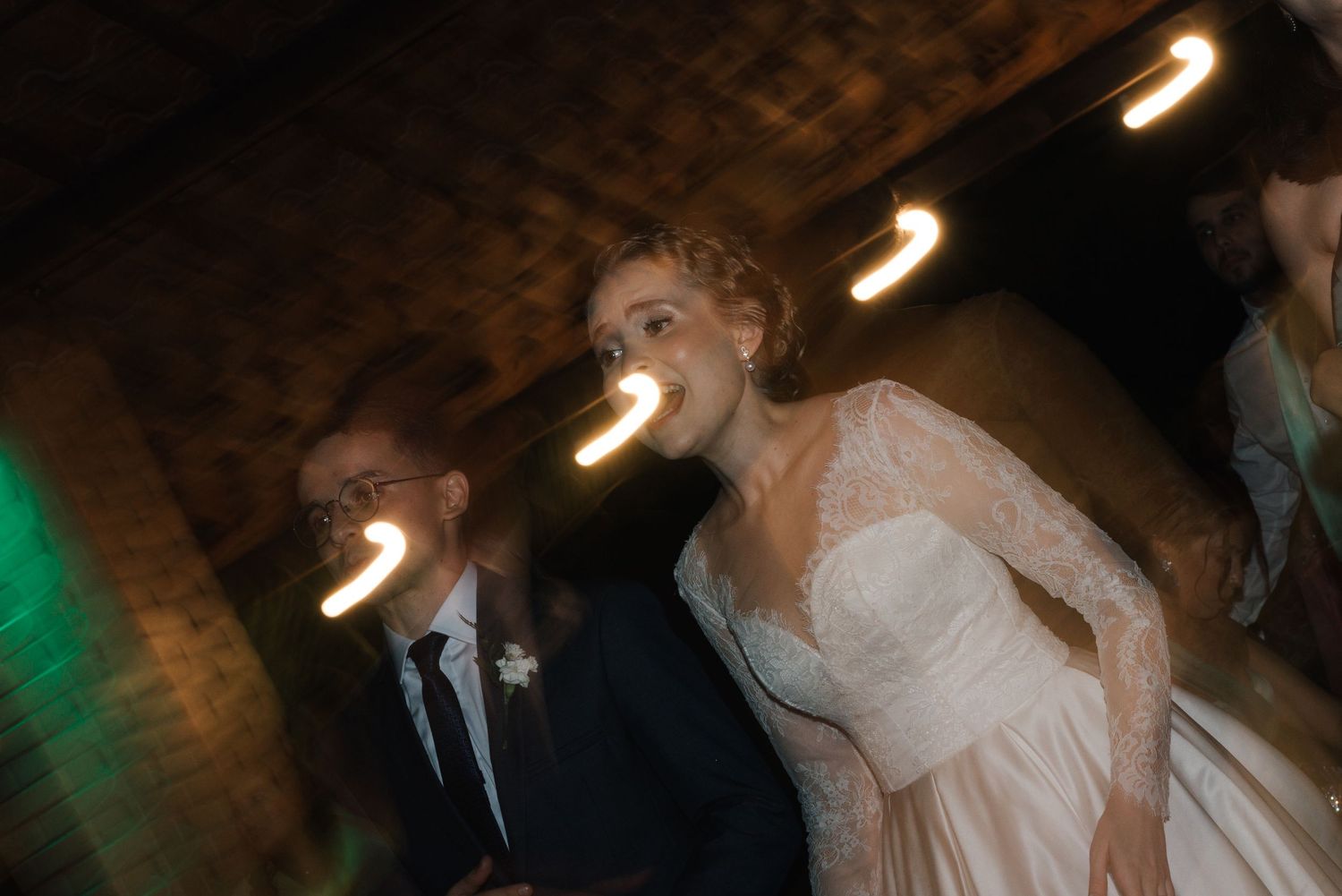 A motion-blur wedding photograph with warm ambient lighting and brick wall background.