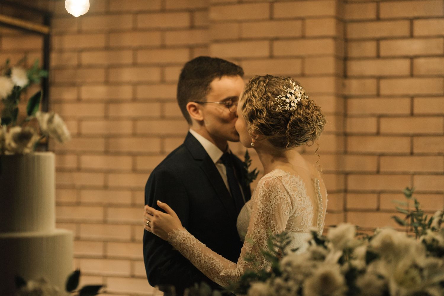 Intimate wedding moment against brick wall with romantic lighting and floral decor.