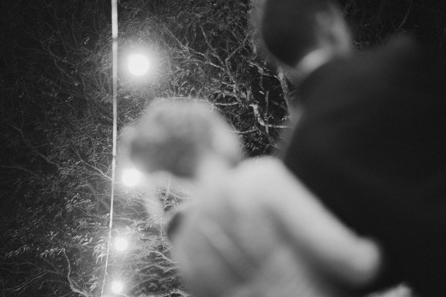 An artistic black and white shot of a wedding couple under string lights.