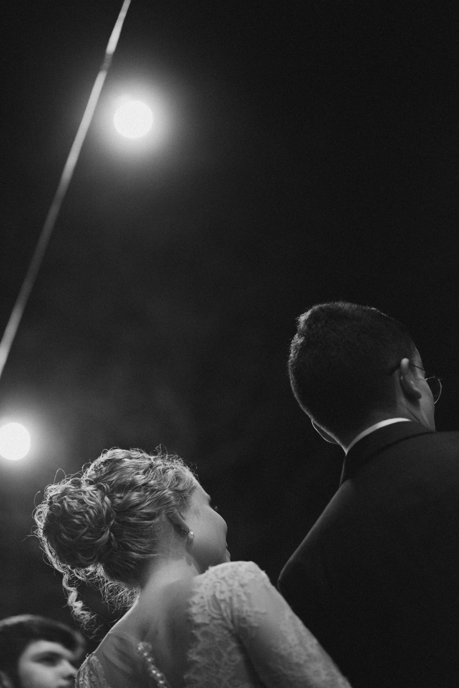 A dramatic low-angle shot of a wedding couple silhouetted against evening lights.