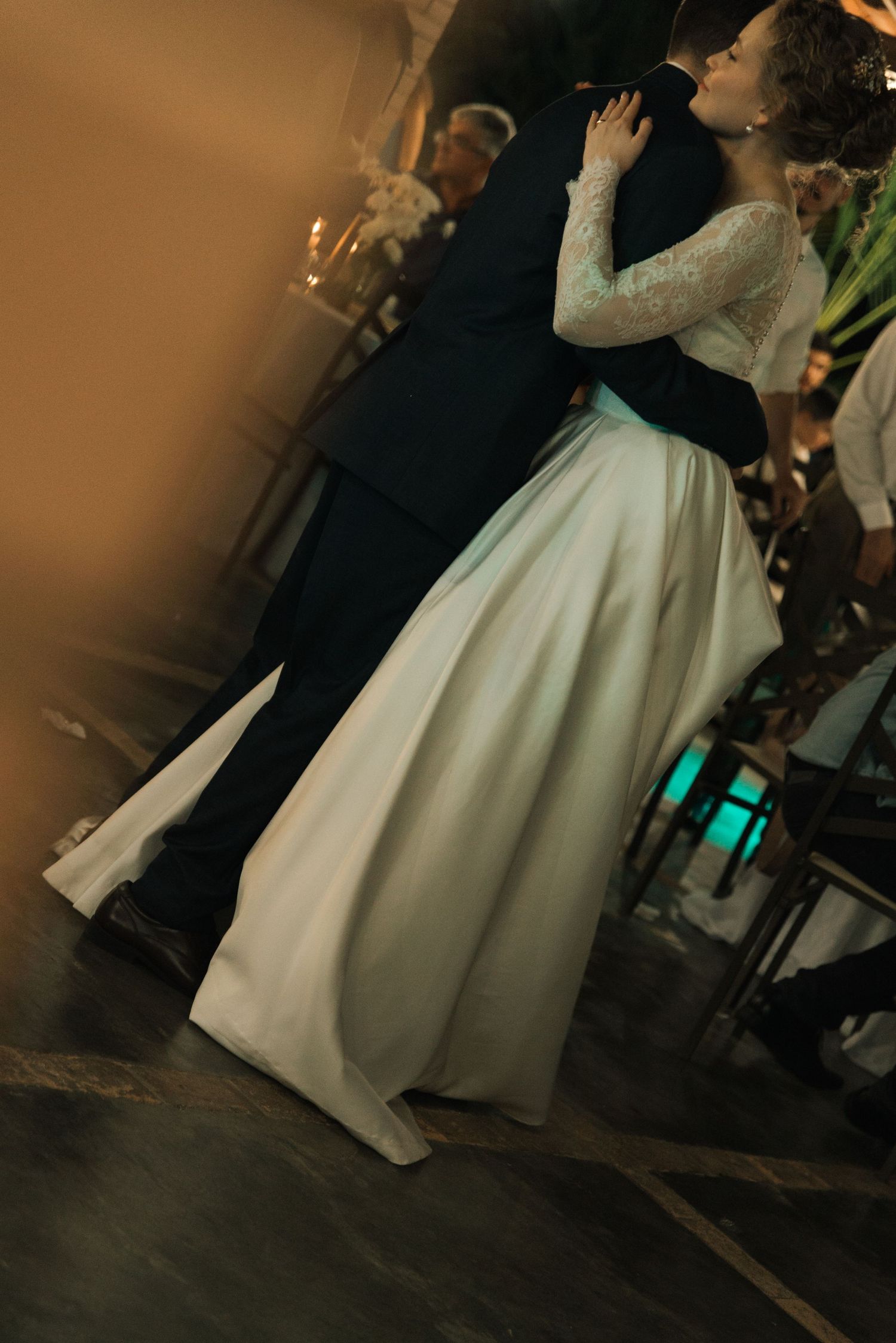 A bride in a flowing white gown with lace sleeves dances at an evening reception.