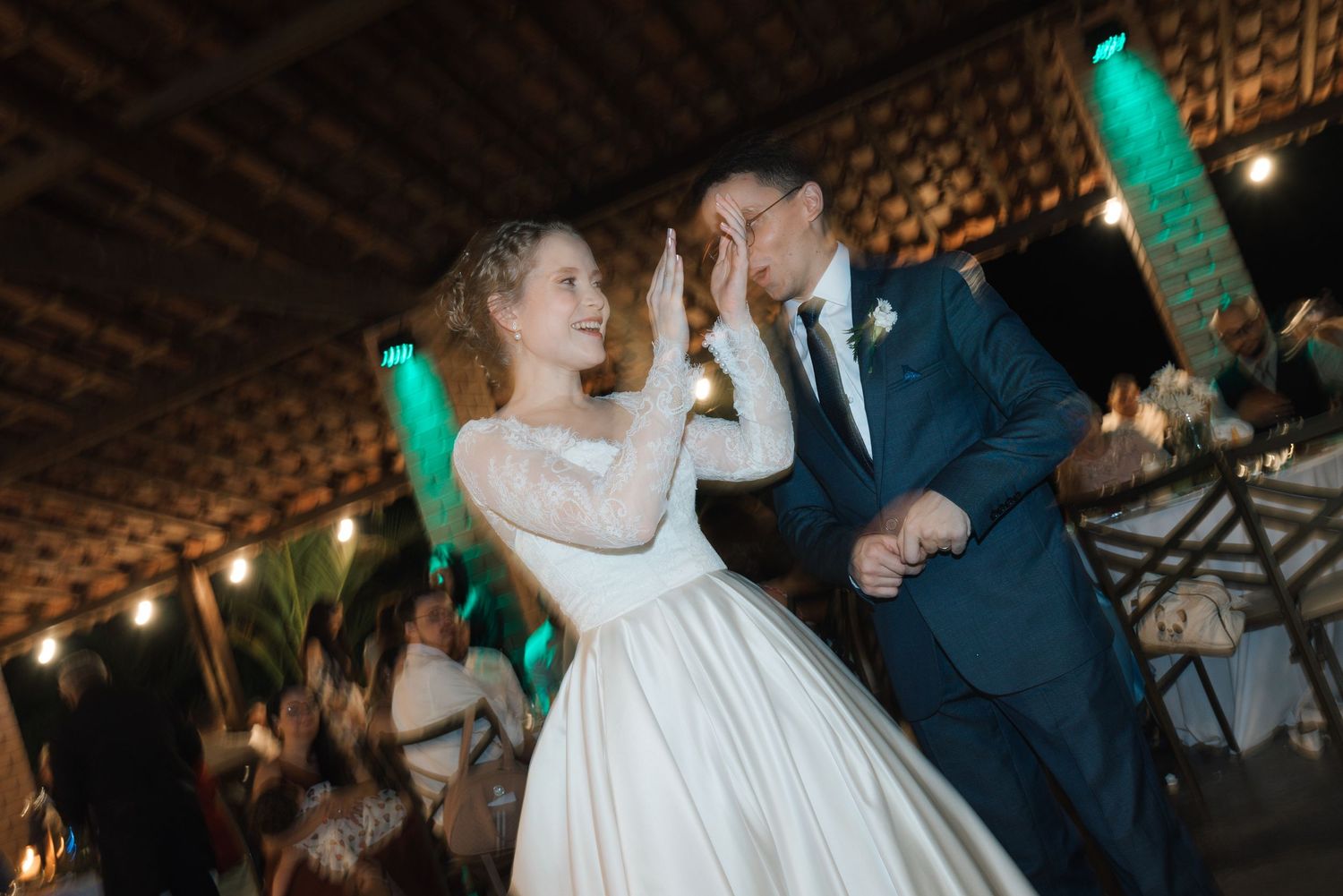 A joyful wedding dance moment under string lights and green ambient lighting.