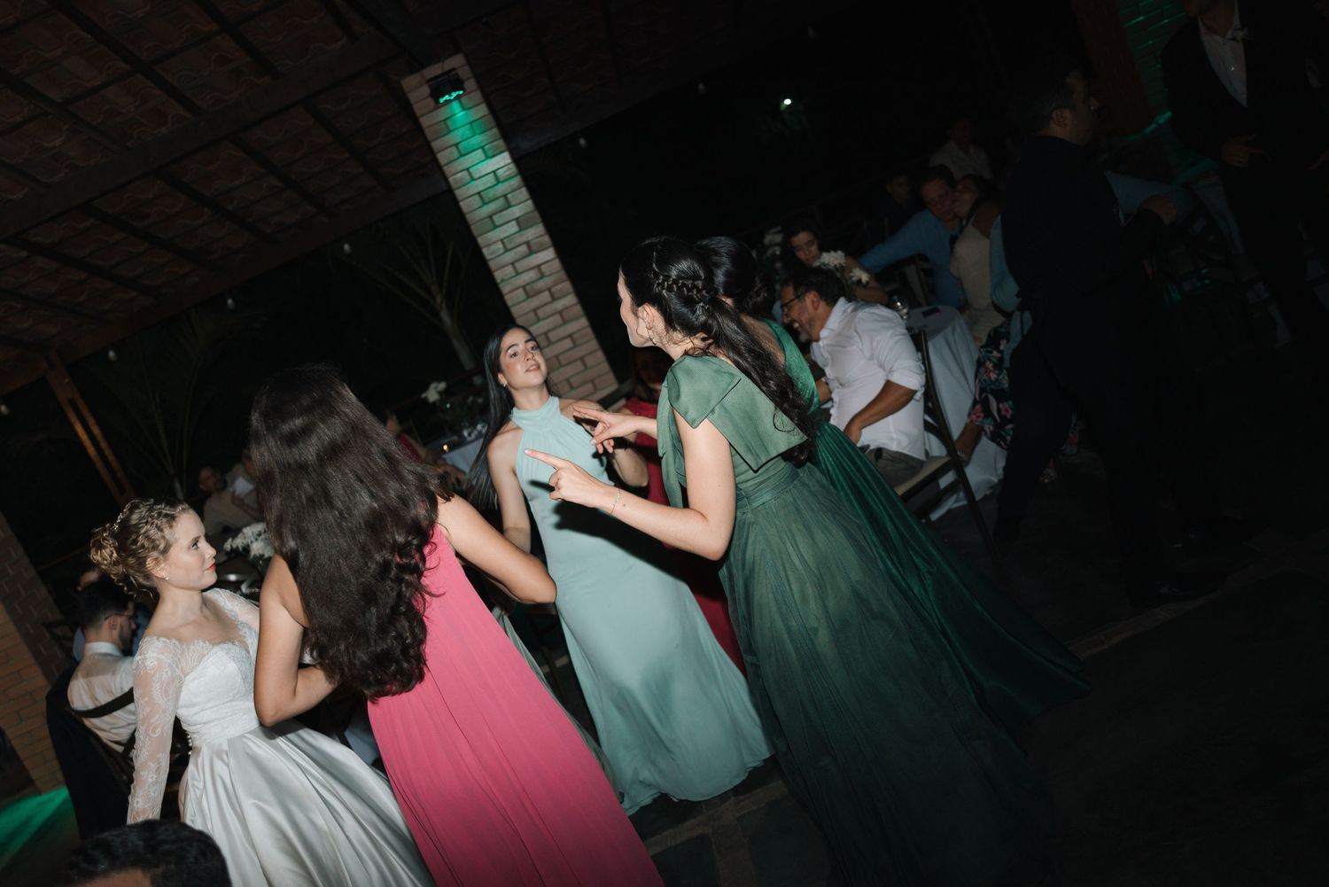 Wedding guests dancing with enthusiasm under green lighting at a dark reception venue.