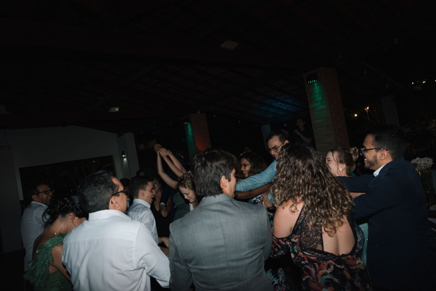 Wedding party and guests celebrating on a dark dance floor with ambient lighting.