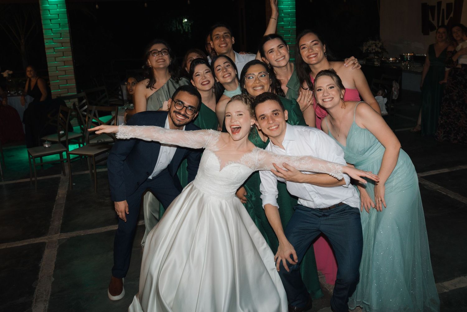 Wedding party strikes playful group pose with bride in classic white gown and bridesmaids in mint dresses.