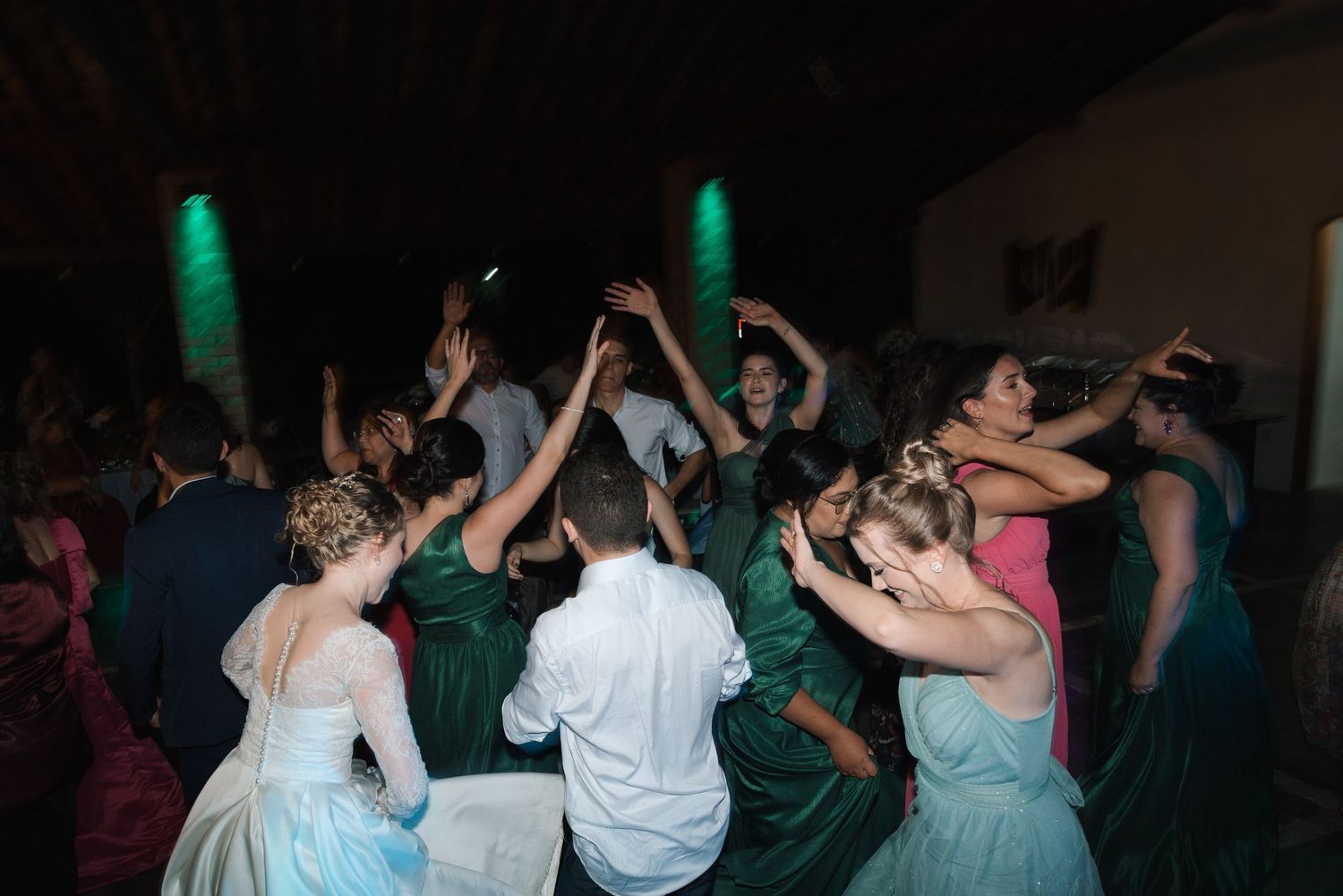 Wedding party dancing in formal attire with green and mint dresses under atmospheric lighting.