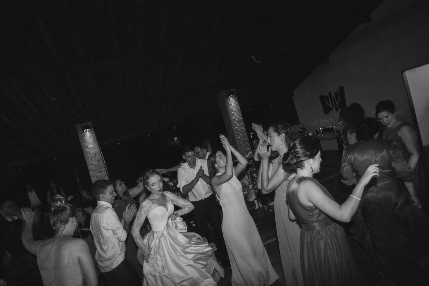 Black and white shot of wedding guests dancing with arms raised at lively reception party.