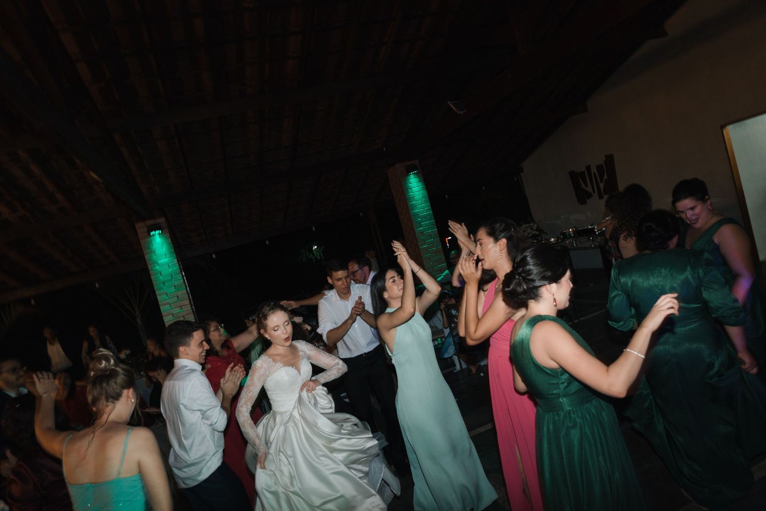 Energetic dance floor scene with wedding guests in formal attire under green venue lighting.