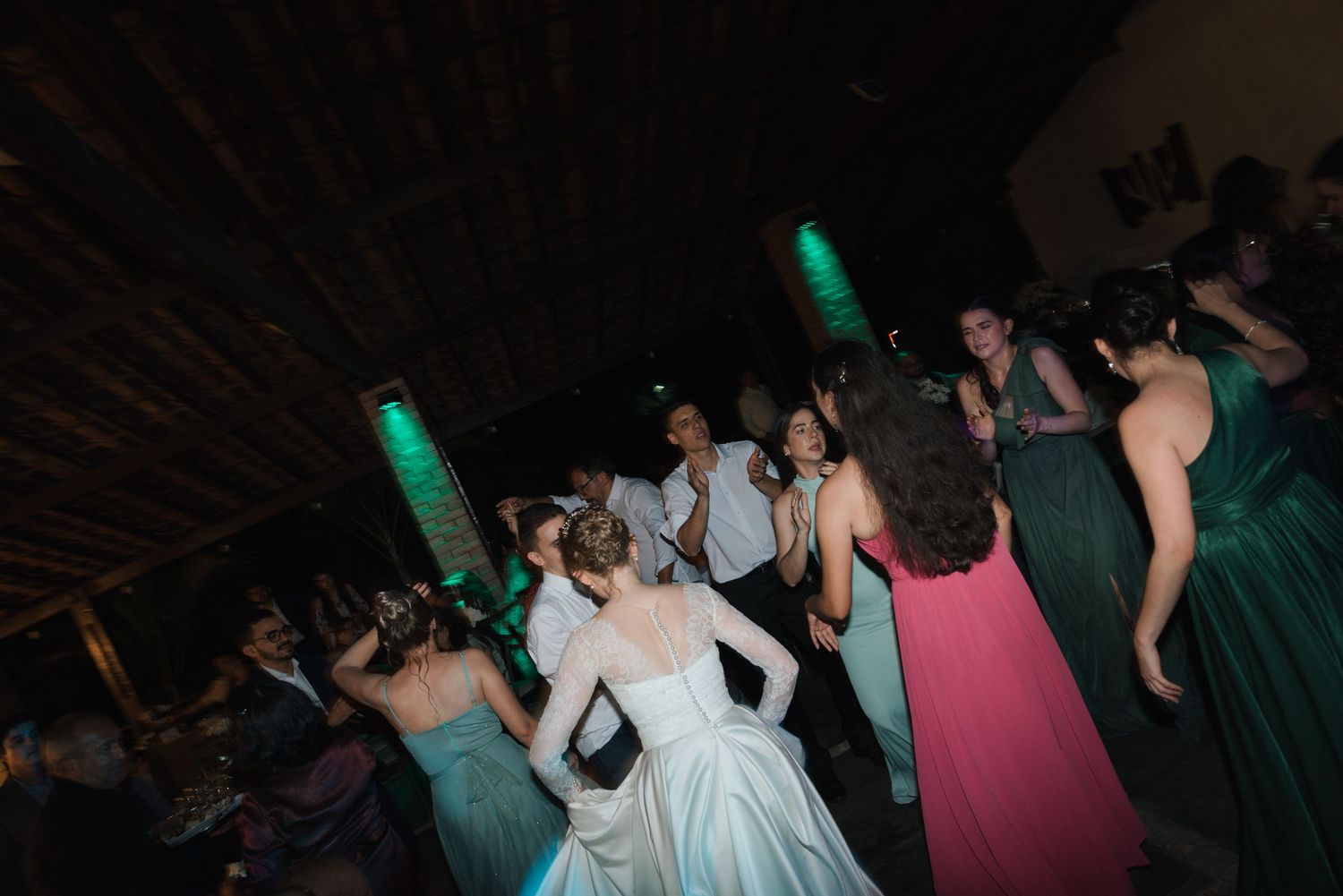 Wedding reception dance floor filled with guests in formal wear under green accent lights.