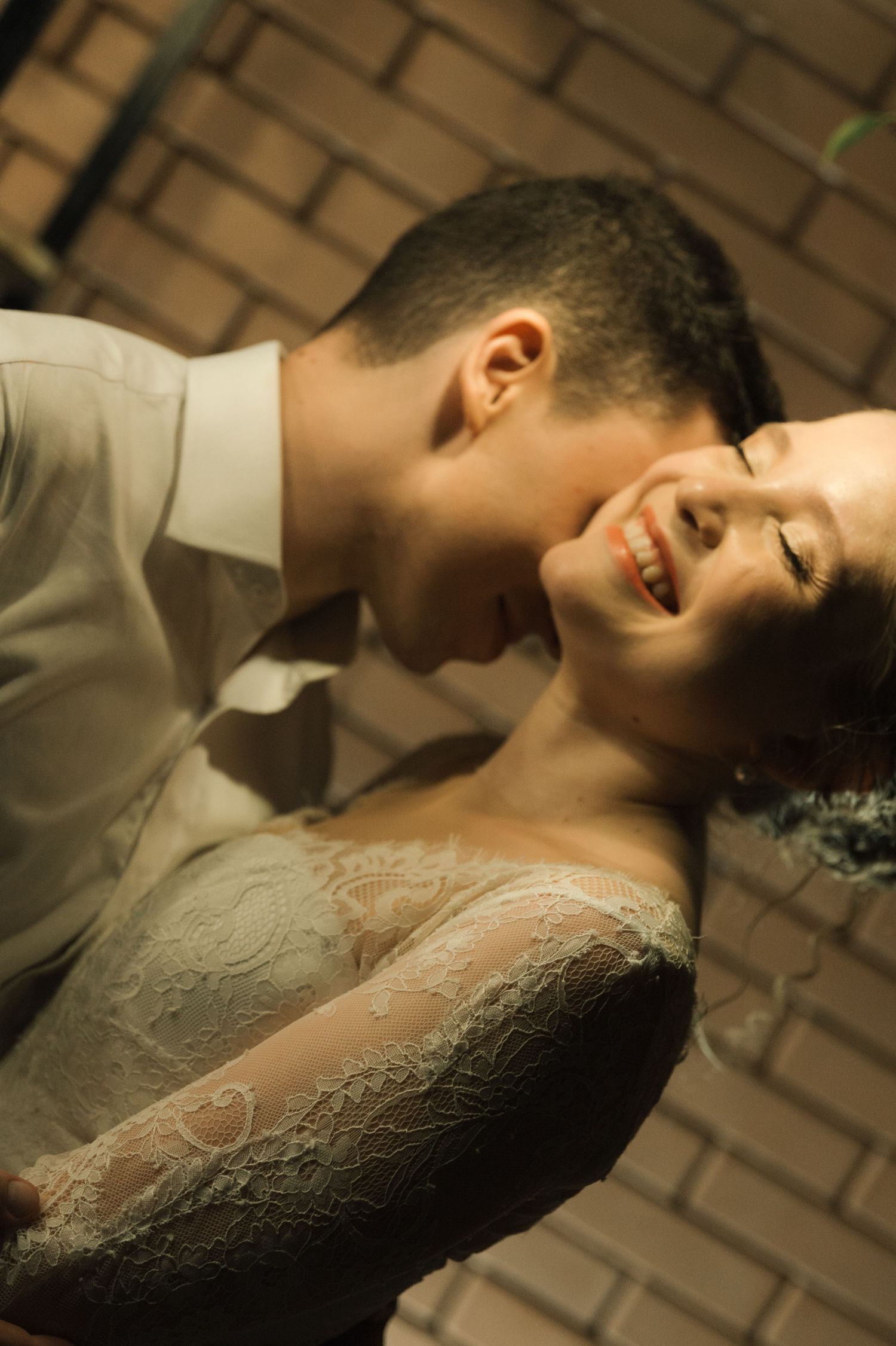 Romantic moment between newlyweds in formal wear embracing against a brick wall background.