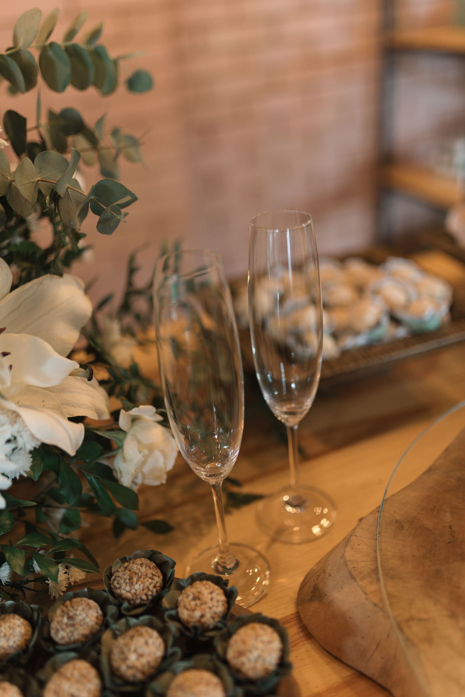 Wedding reception detail with champagne flutes, eucalyptus, and desserts on wooden table.