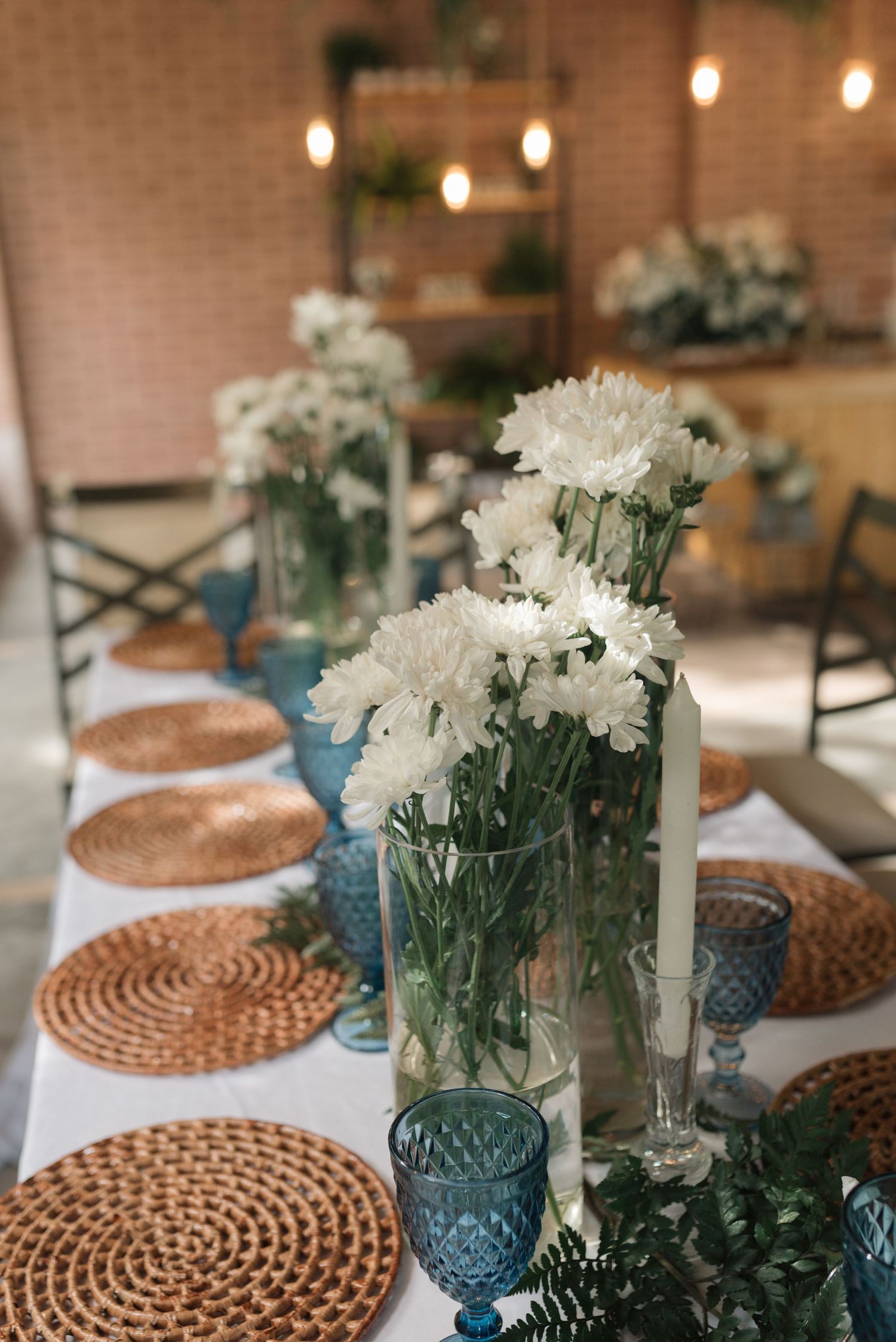 Wedding table setting with blue glass vases, white flowers, and woven placemats.