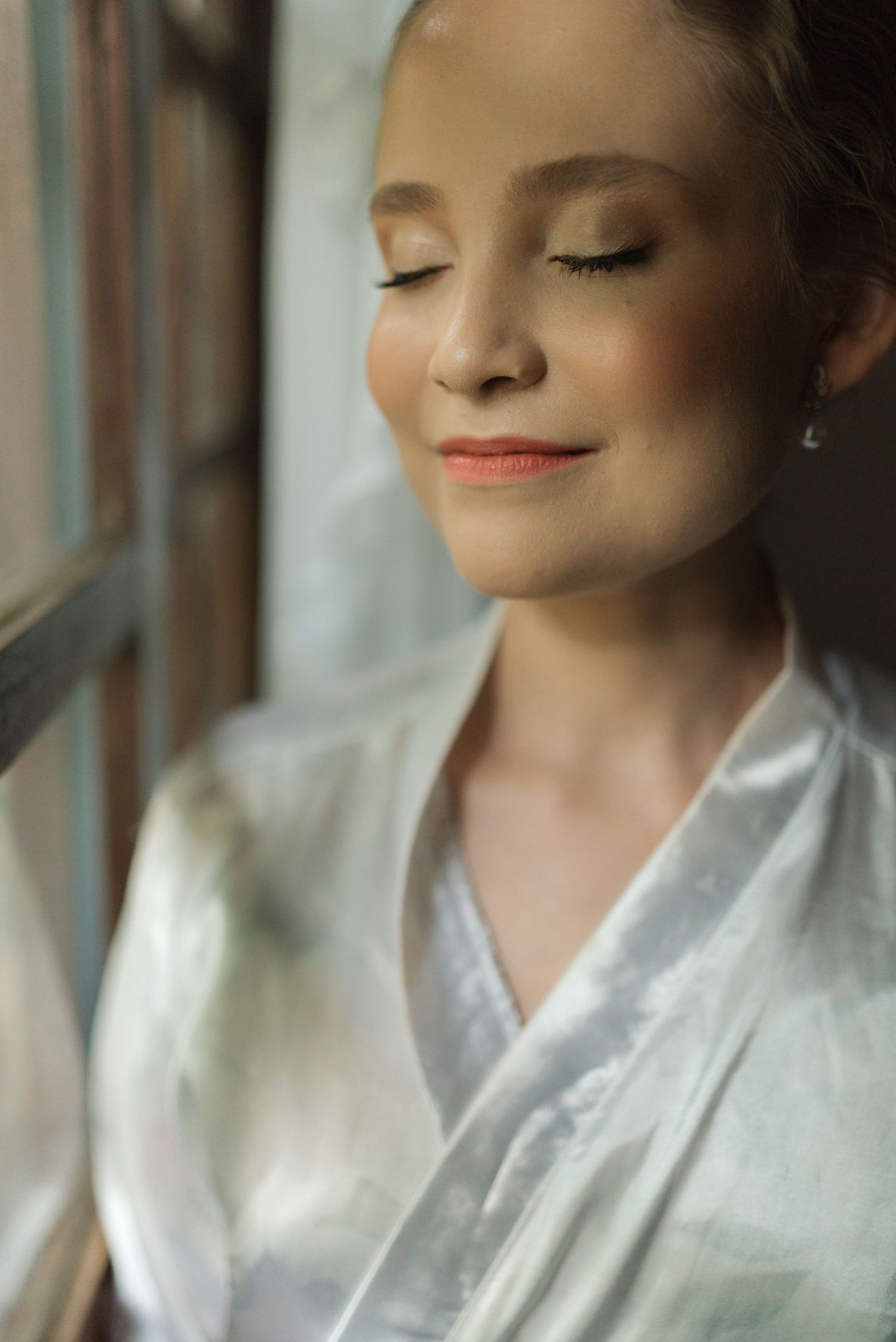 Serene portrait of someone in white robe by window with soft natural lighting.