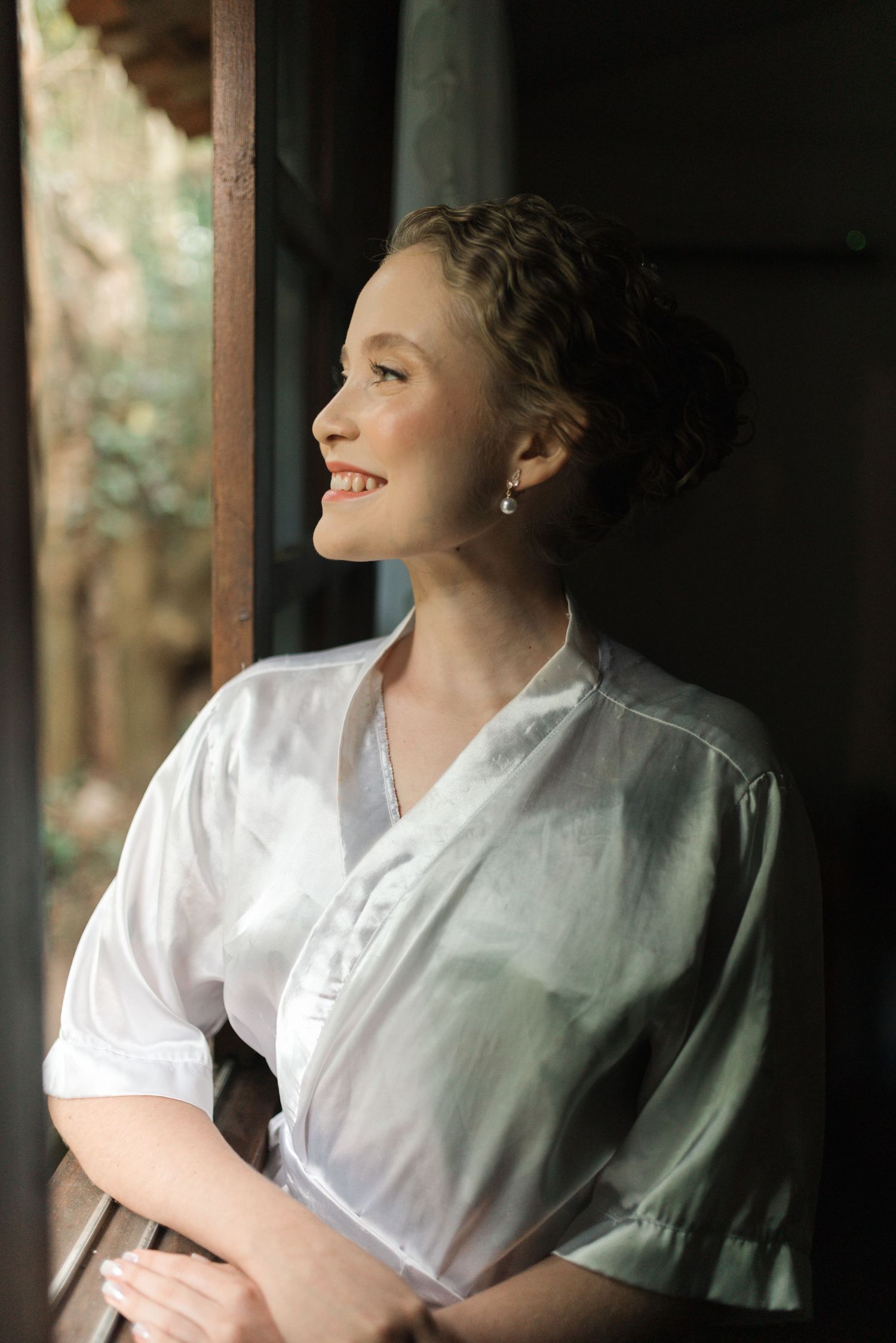 Portrait by window showing joyful expression while wearing white robe.
