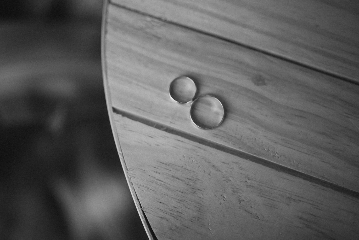 Close-up black and white image of two wedding rings on a wooden surface.