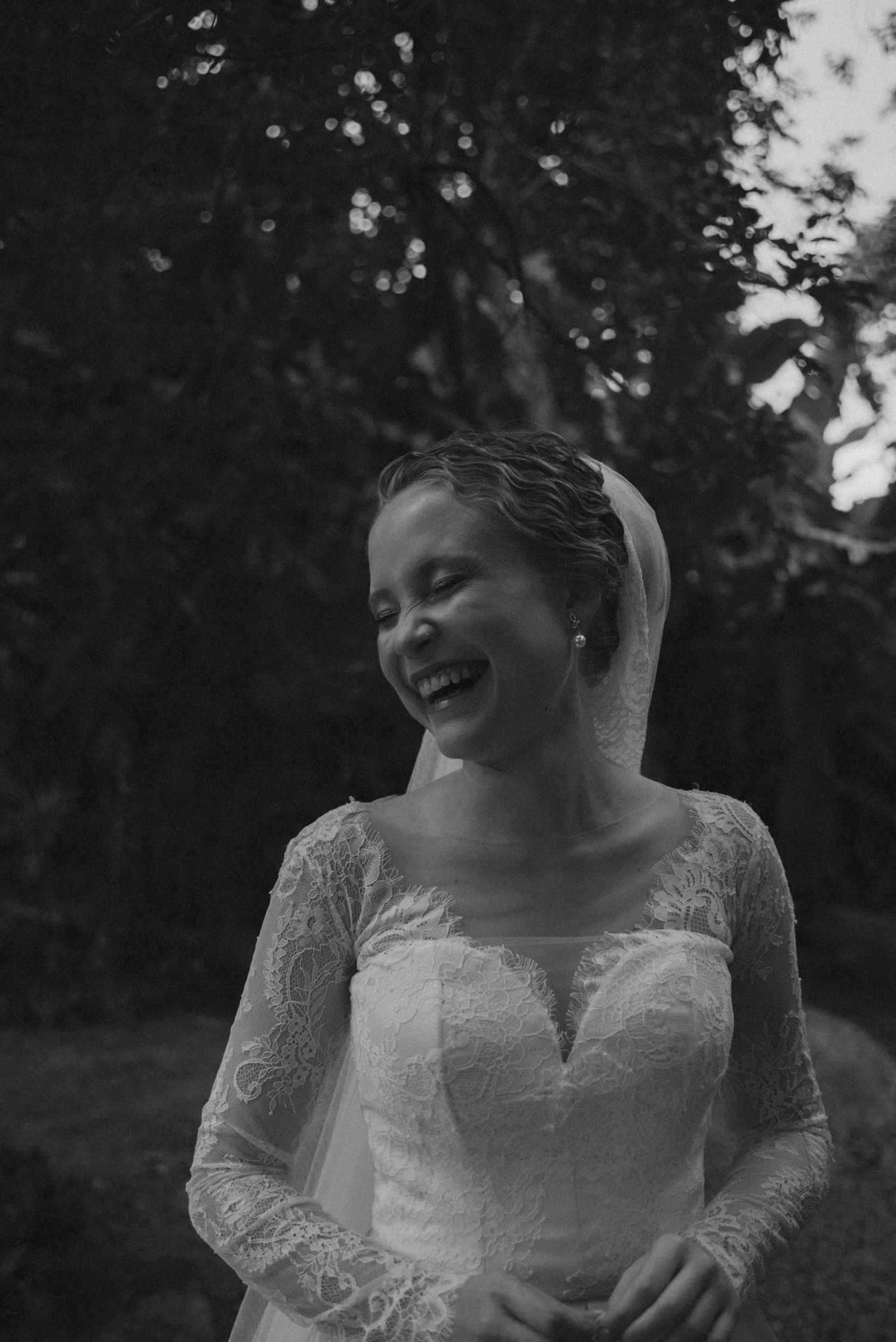 Candid black and white photo of a bride in lace wedding dress outdoors.