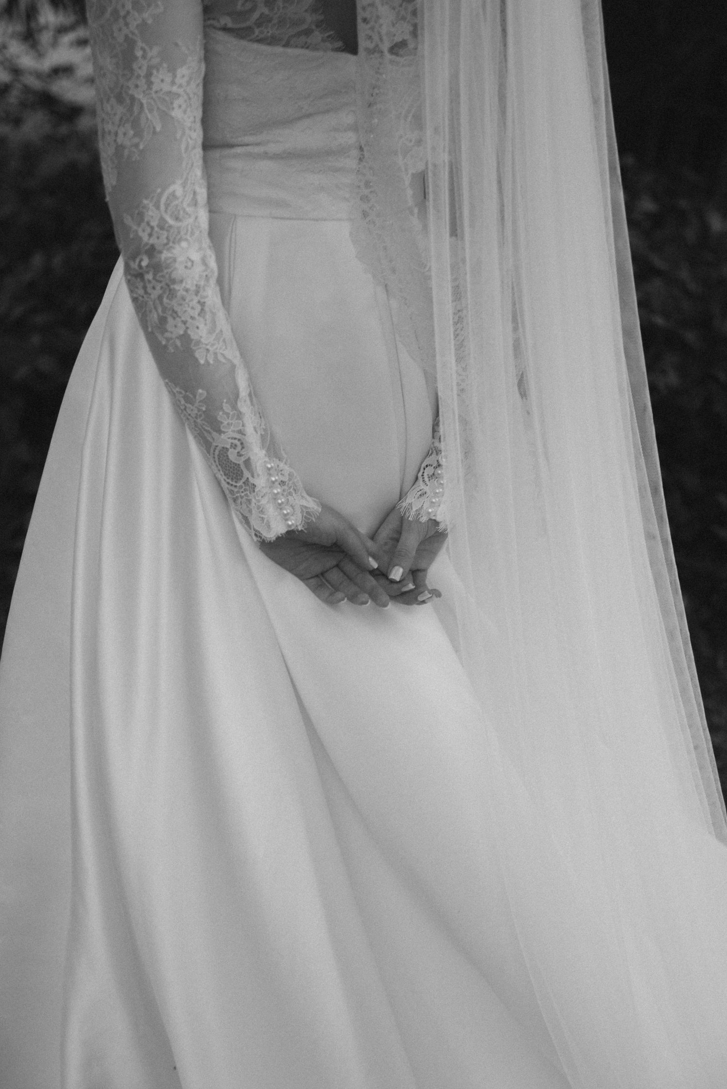 Black and white detail shot of lace sleeve and flowing wedding dress fabric.